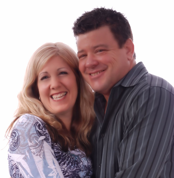Smiling couple, woman with long blonde hair and man with short dark hair, close together against a white background.