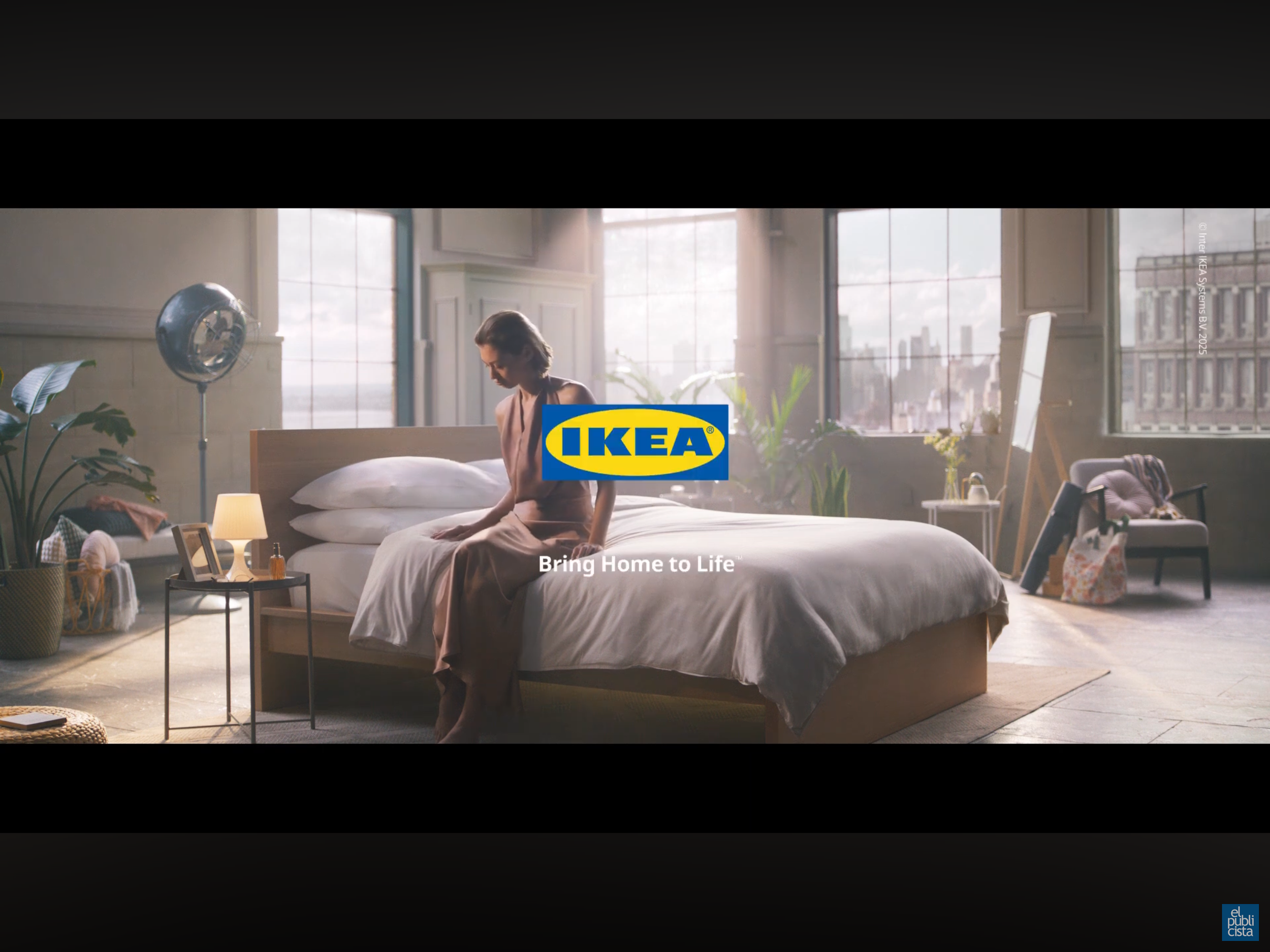 A woman sitting on a bed in a bright, spacious bedroom with large windows, plants, and furniture, featuring the IKEA logo and slogan 'Bring Home to Life'.