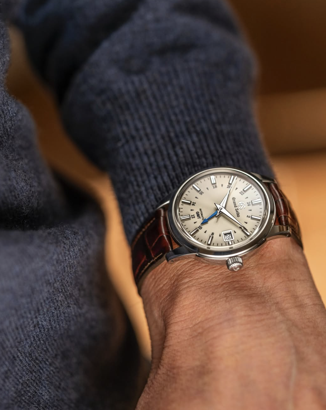 Close-up of a person's wrist wearing a Grand Seiko wristwatch with a brown leather strap, silver dial, and multiple subdials, showing the time and date.