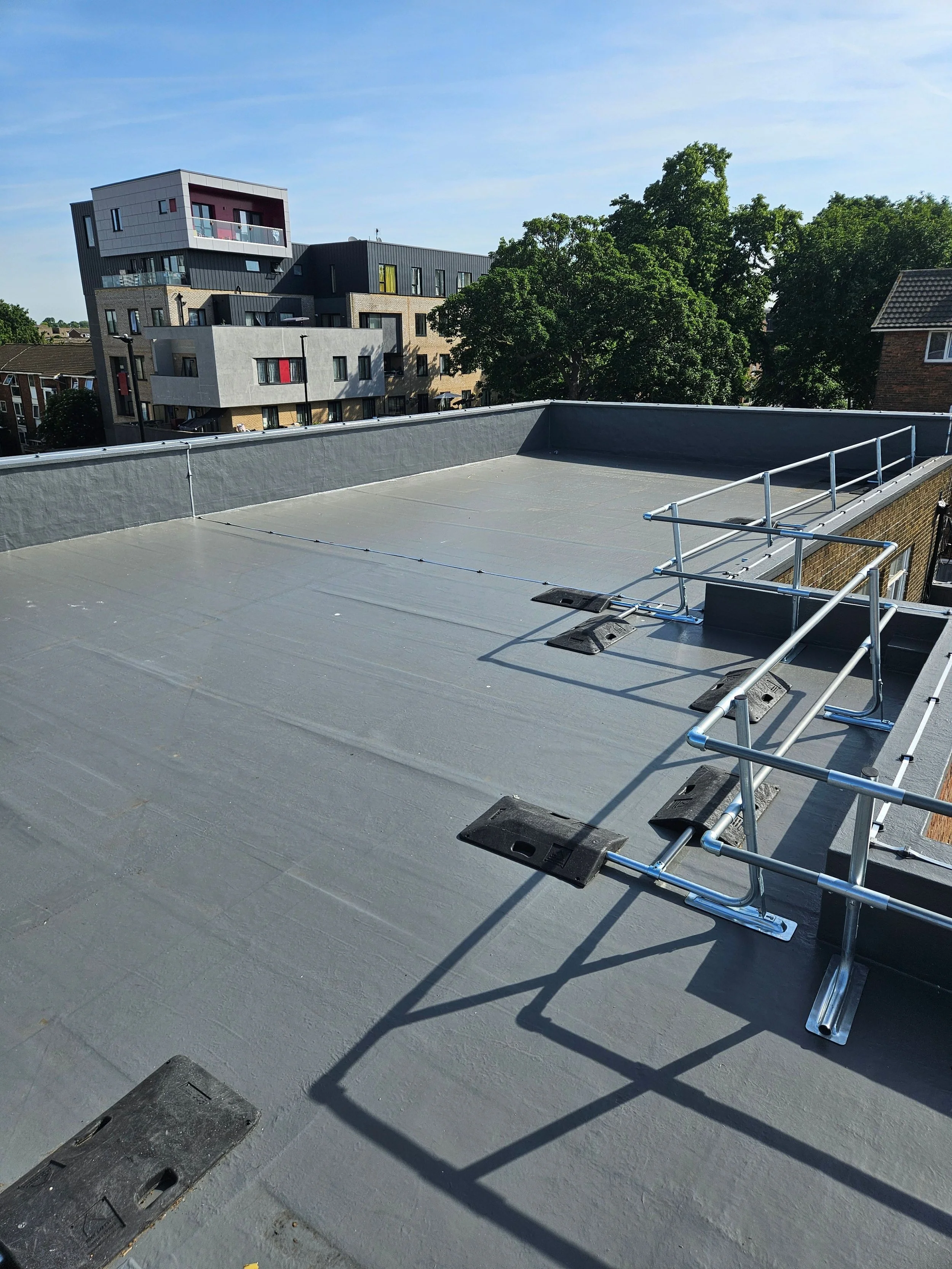 Large flat roof with grey liquid waterproofing applied with buildings and green trees in the background.