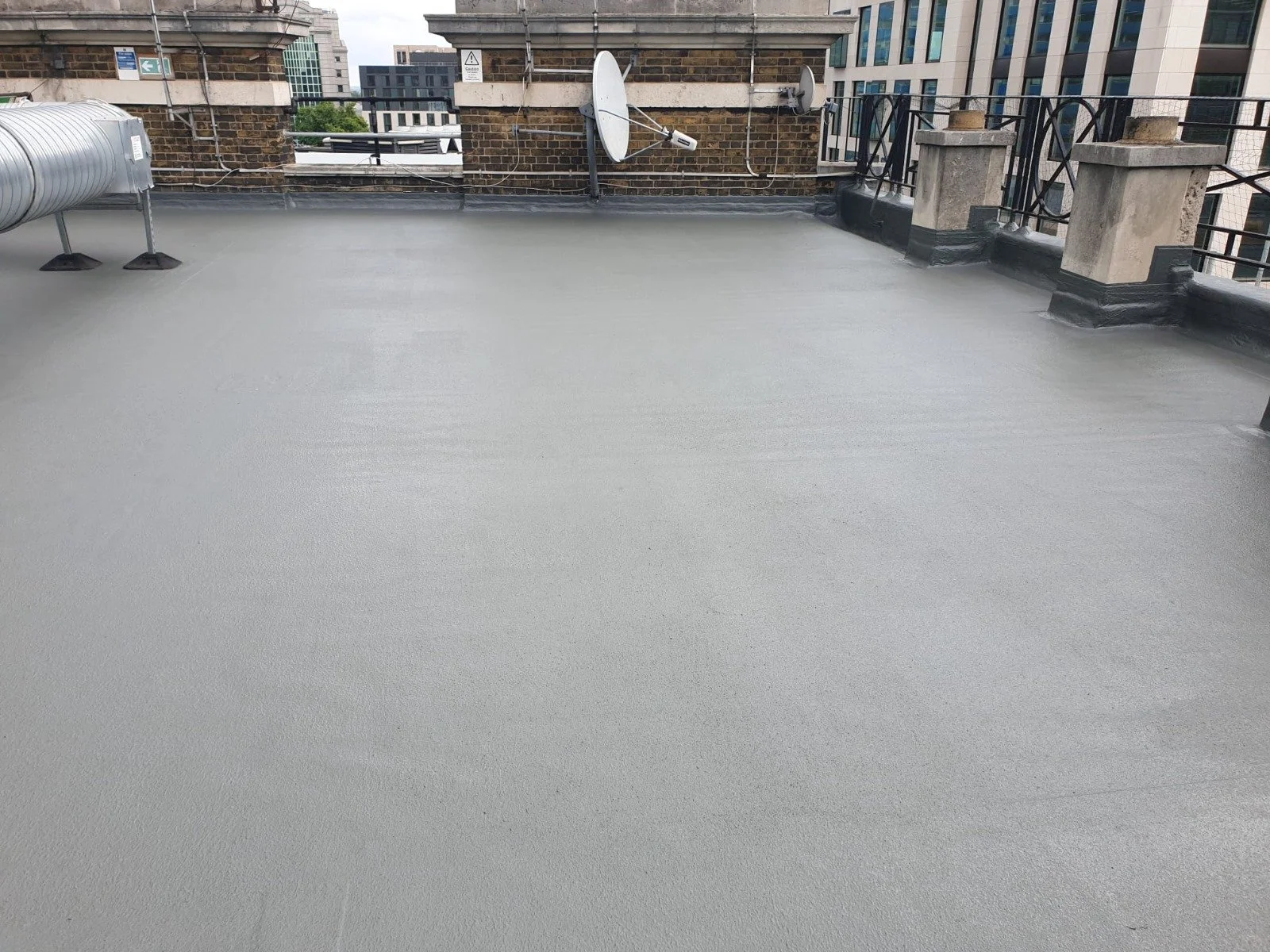 Flat roof with smooth grey waterproofing topcoat, surrounded by railings and plinths