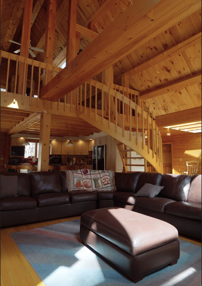 Living room with leather sectional sofa, a window in the background, and wooden interior with a staircase leading to an upper level.