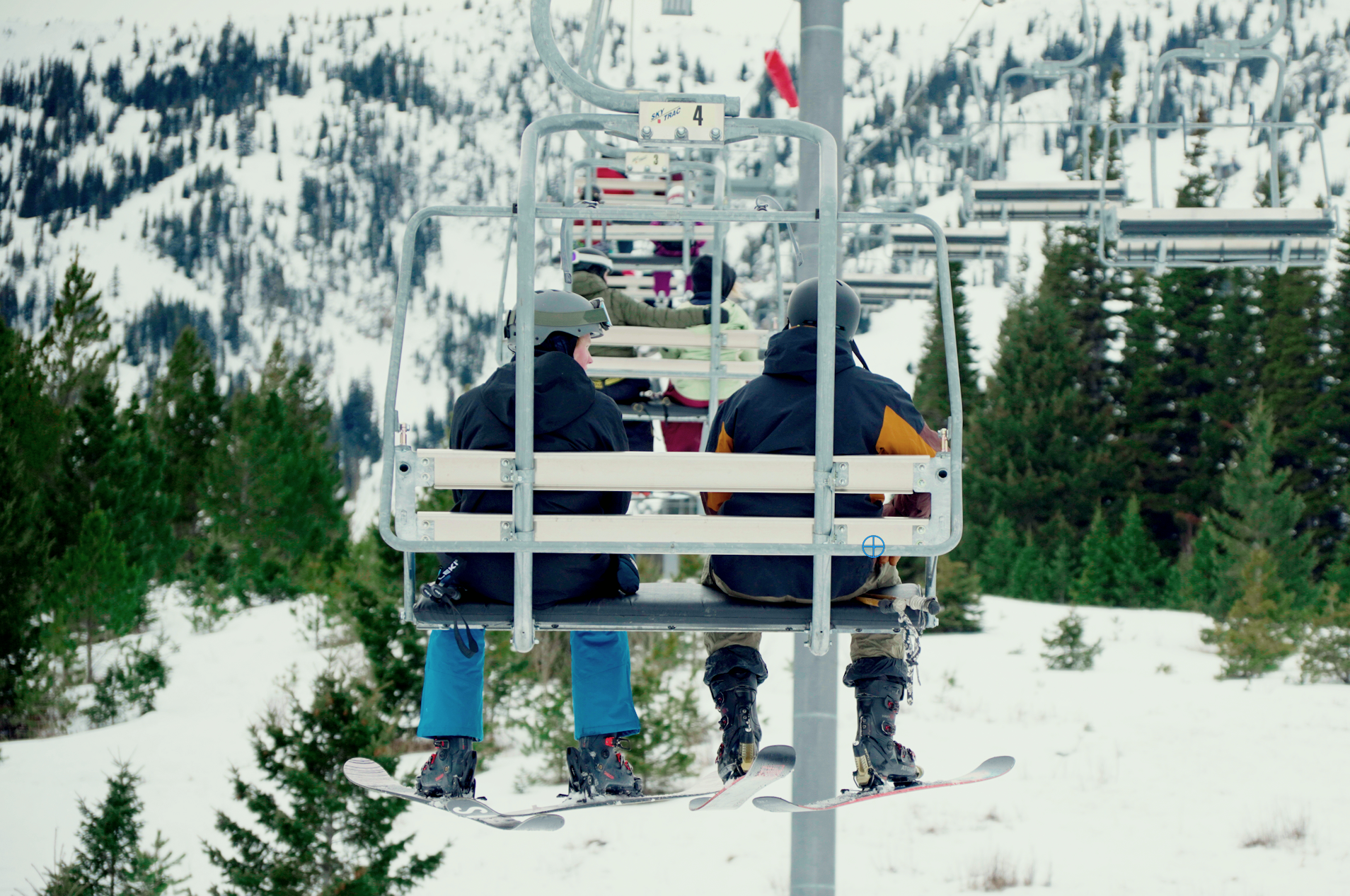 People riding ski lift over a snowy mountain with evergreen trees.