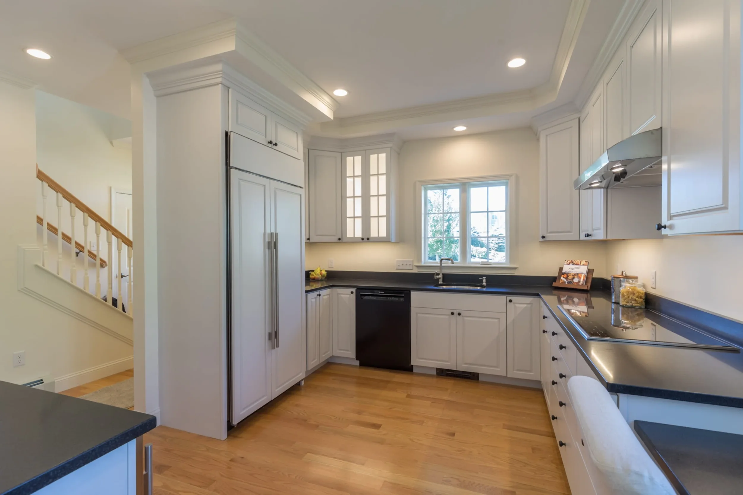 Modern kitchen with white cabinets, black countertops, natural wood flooring, and a window above the sink.