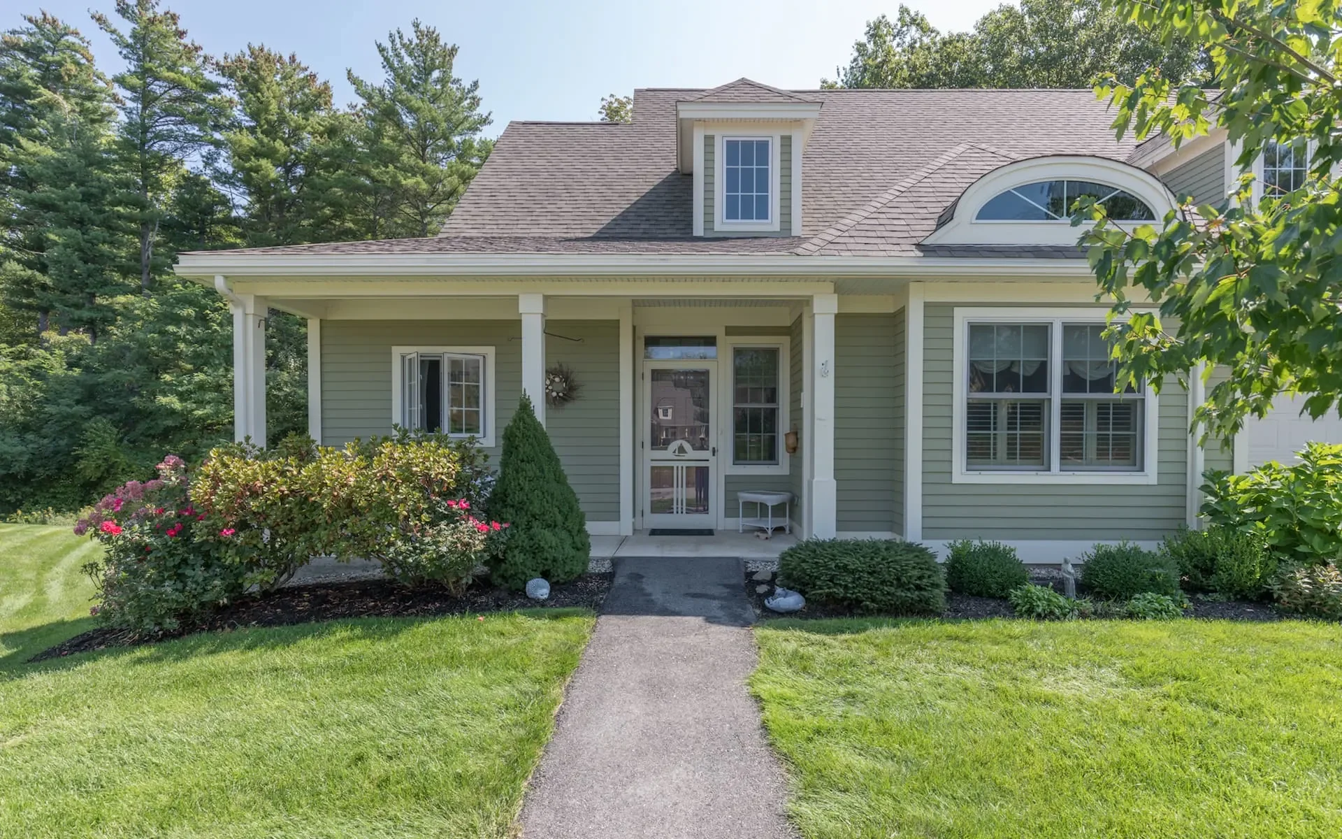 Front view of a two-story house with beige siding, a porch, and a landscaped front yard with bushes and flowerbeds.