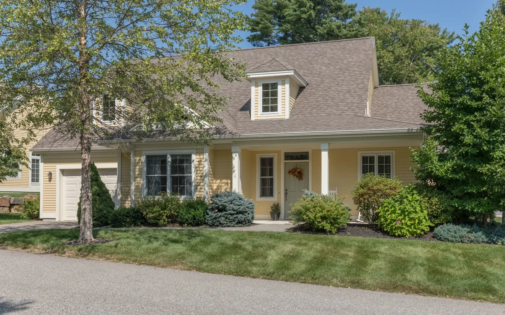 Yellow house with a front porch, landscaped yard, and trees in a suburban neighborhood.