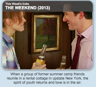 Scene from the movie The Weekend (2013) showing two young adults at a reunion, holding drinks, in a cozy indoor setting with a framed landscape painting on the wall.