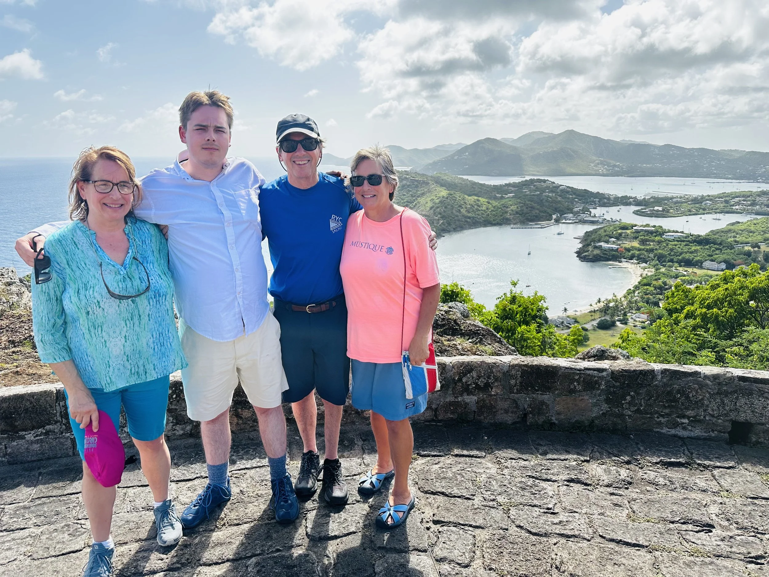 Four people standing on a stone platform with a bay and mountains in the background, smiling and posing together.