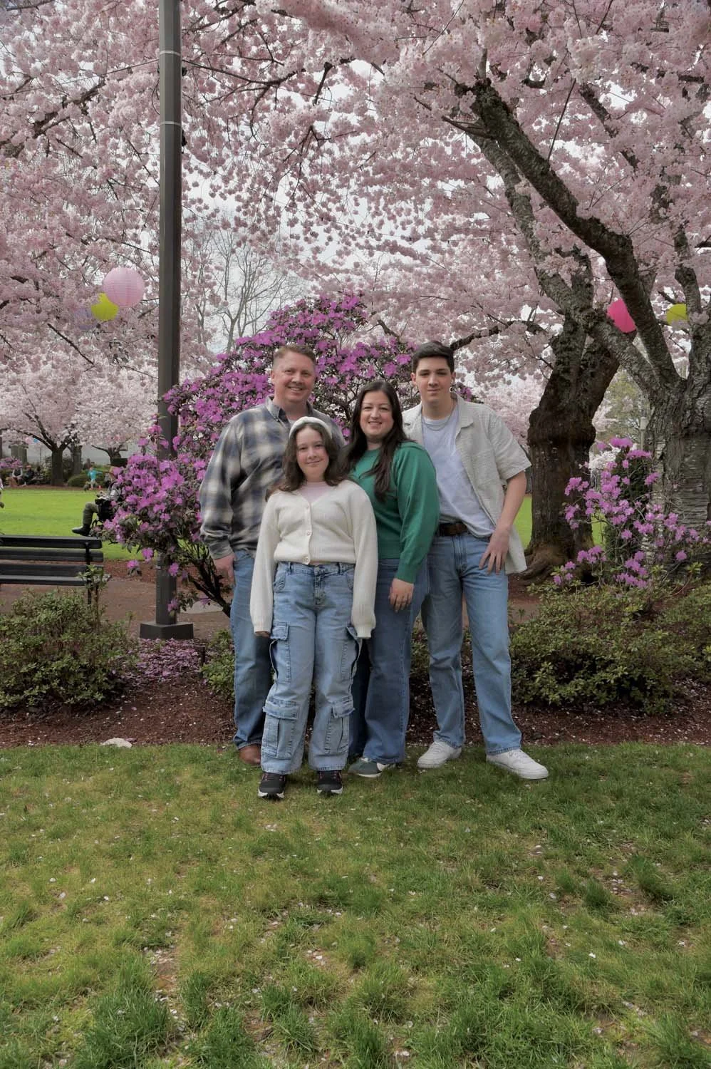 Michael Welsh and his Family, a Group of four people standing under pink cherry blossom trees in a park during daytime.
