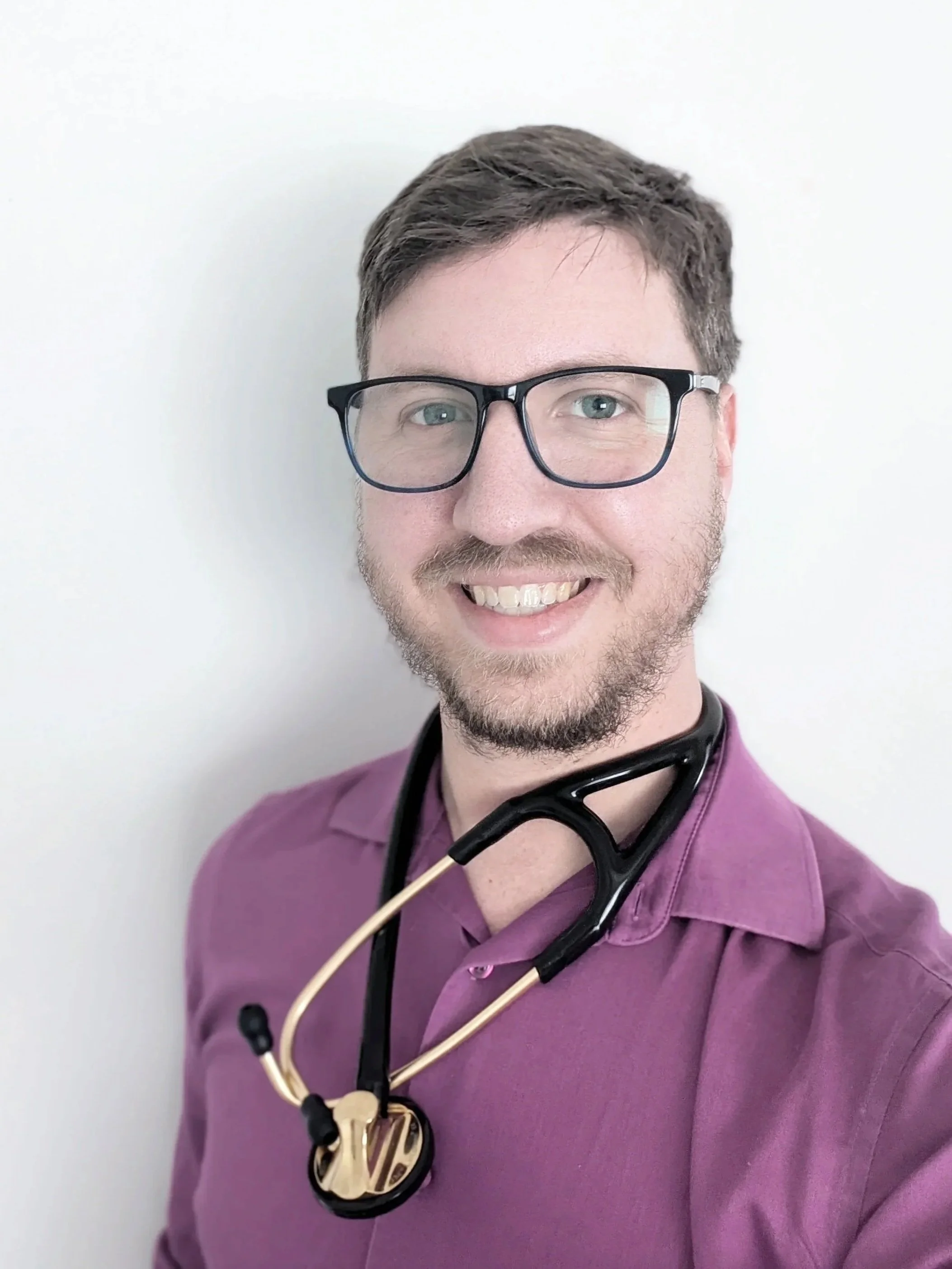 White male with blue eyes wearing glasses, a stethoscope and smiling at the camera