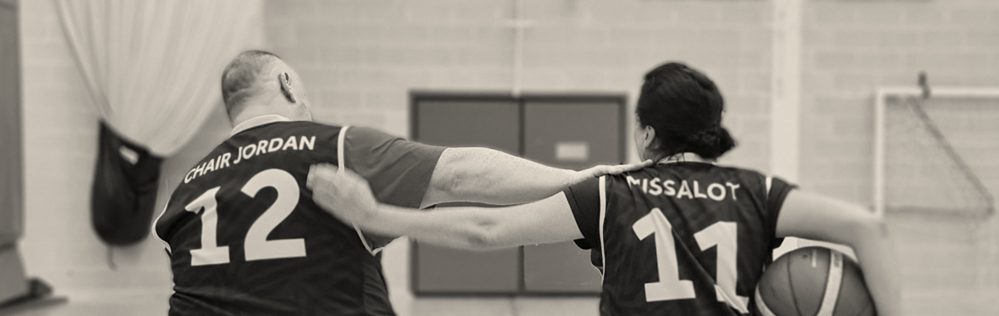 Two basketball players in jerseys, one labeled 'Chair Jordan 12' and the other 'Missalot 11', appear to be celebrating or comforting each other in a gymnasium, with a basketball in the background.
