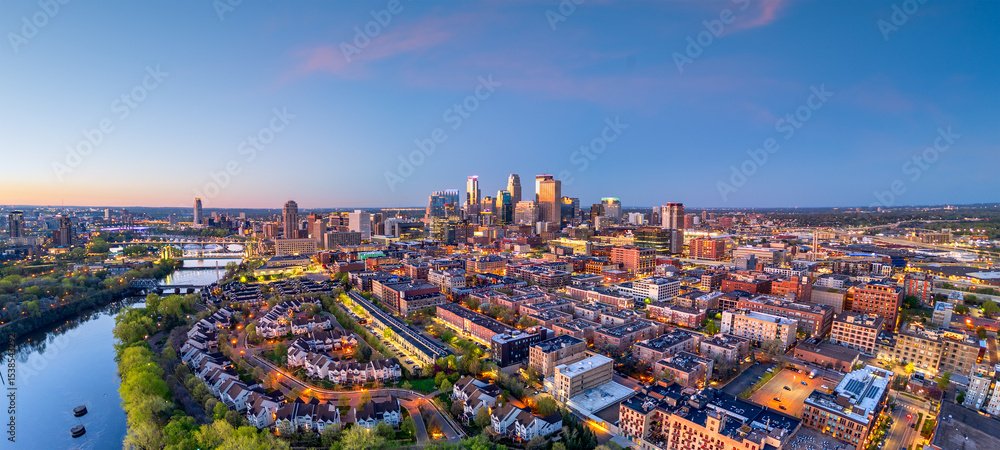 Aerial view of downtown Minneapolis at sunset with city buildings, residential areas, and a river.