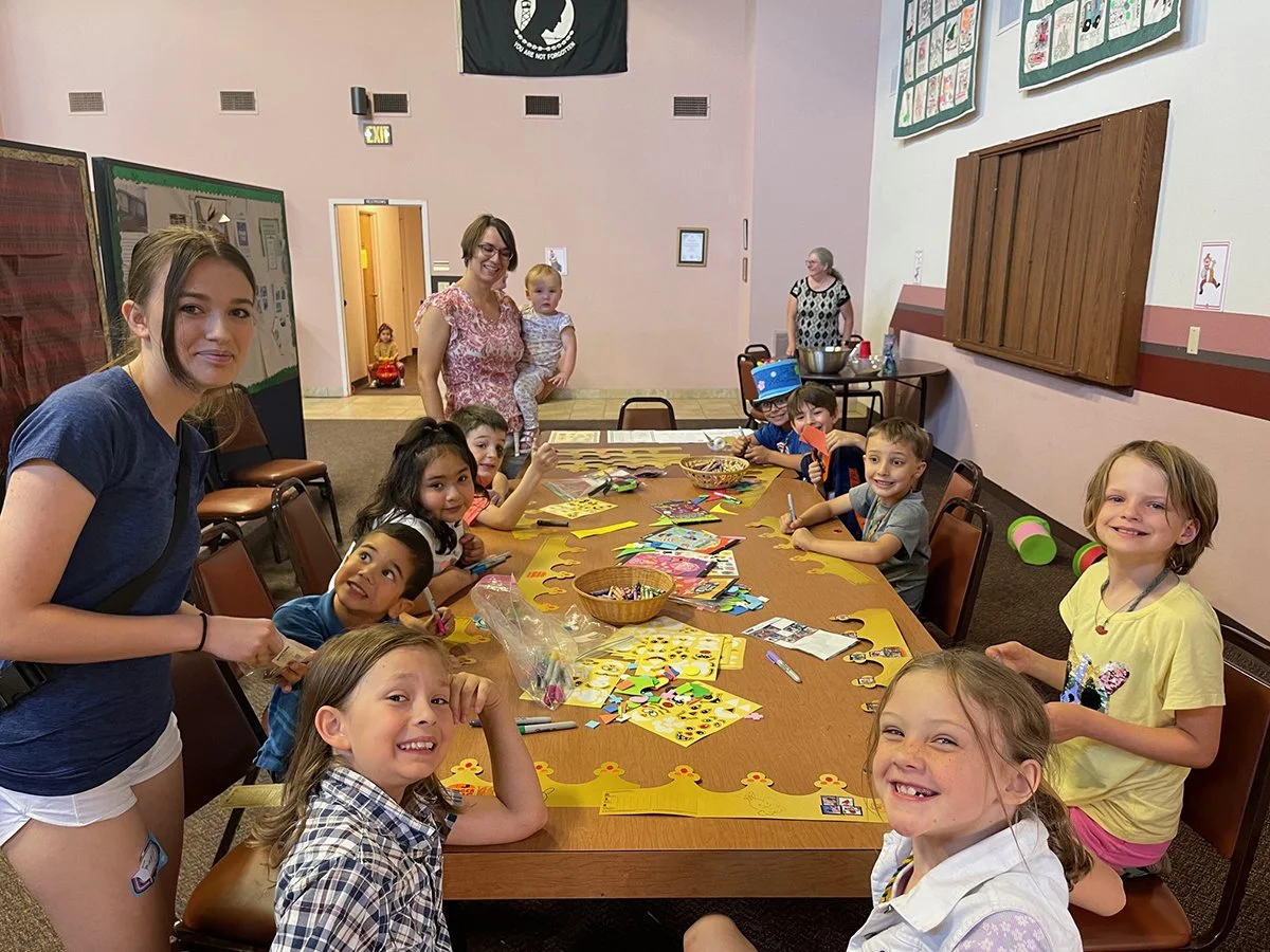 Children's Ministry - children and adults gathered around a table, engaged in arts and crafts activities.