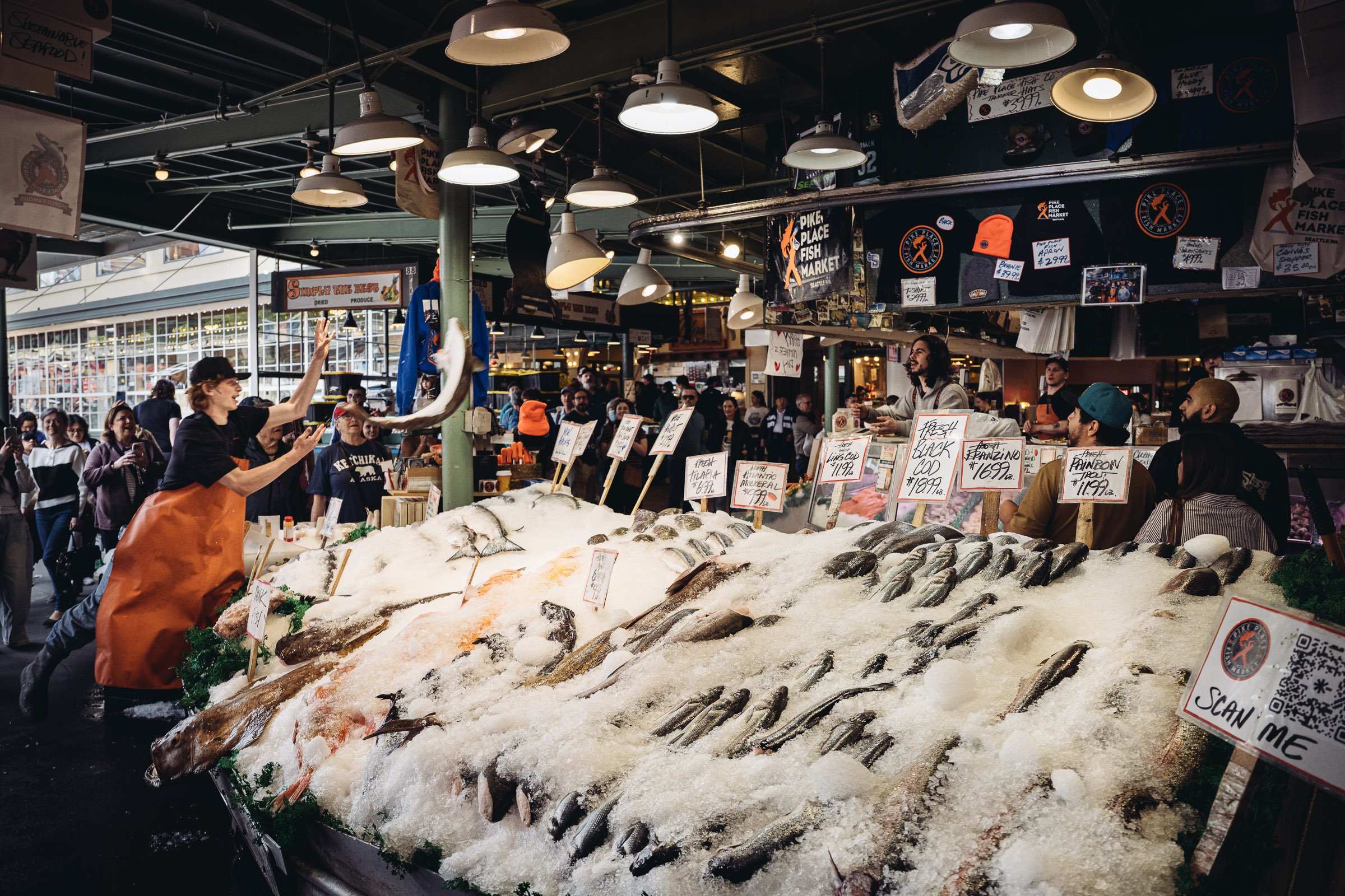 Fresh fish on ice at a seafood market, with shoppers and vendors in the background.