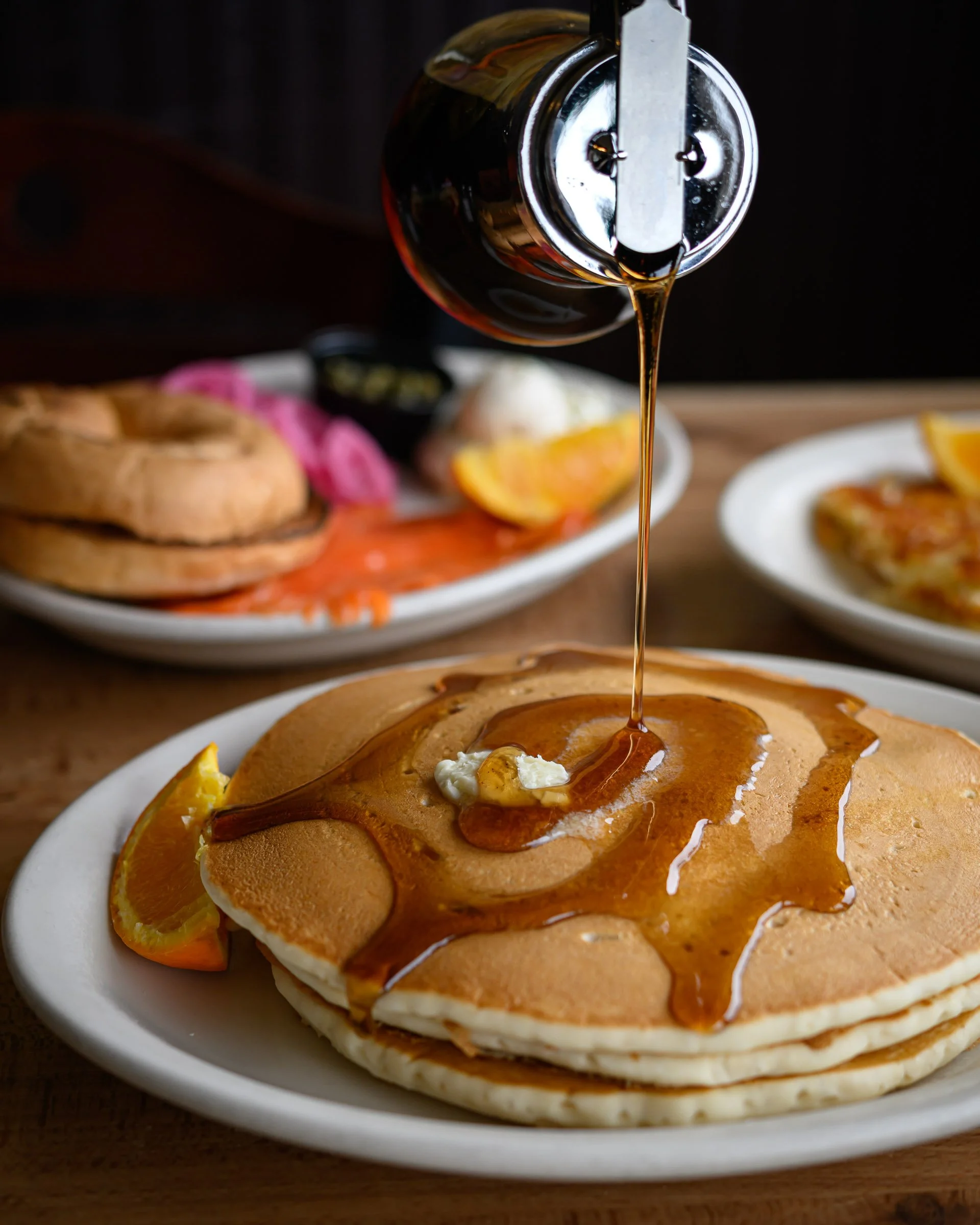 Pancakes with syrup and butter, garnished with lemon slices on a white plate.