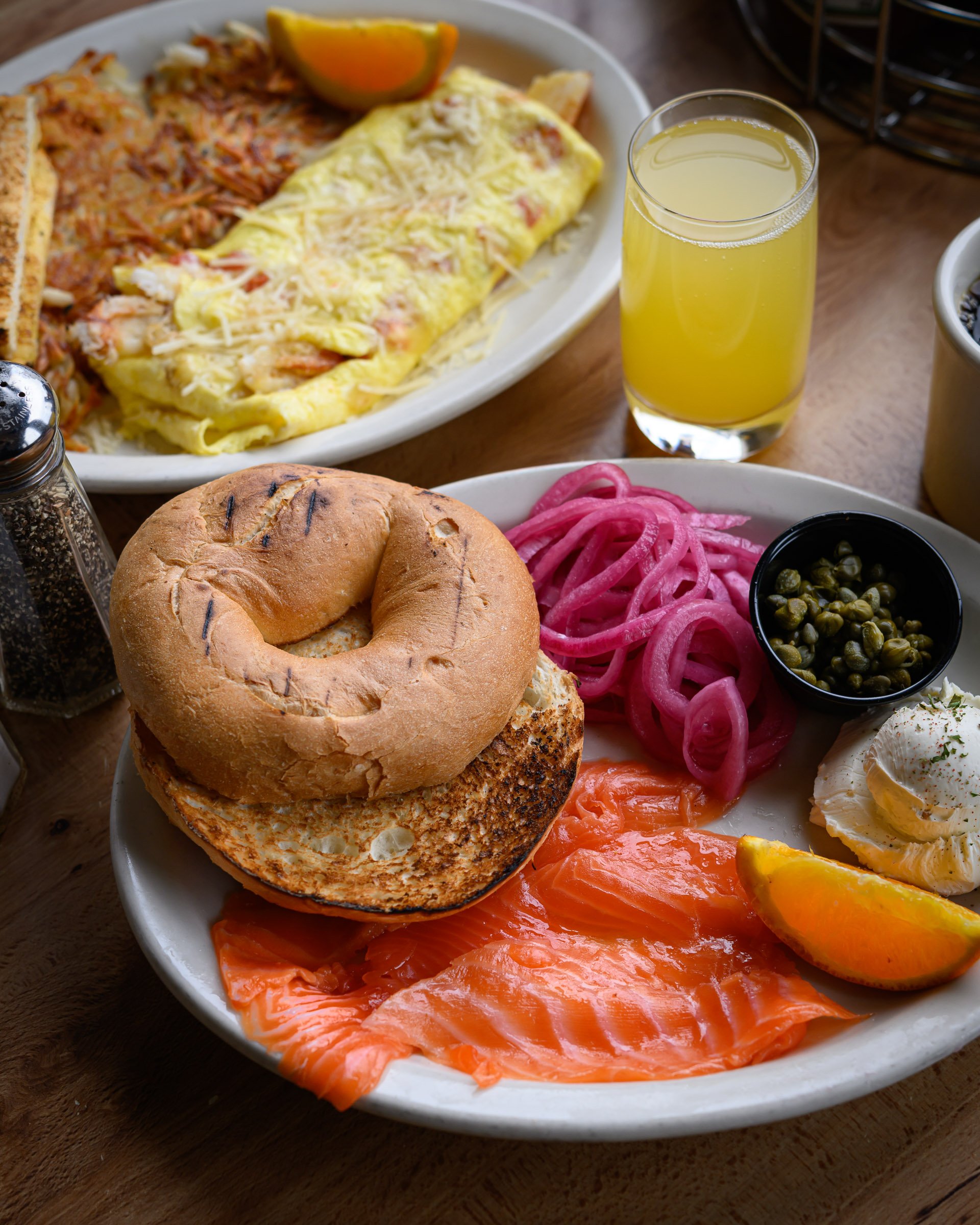 A breakfast plate with smoked salmon, bagel, pickled red onions, eggs, and lemon wedge, along with a glass of orange juice.