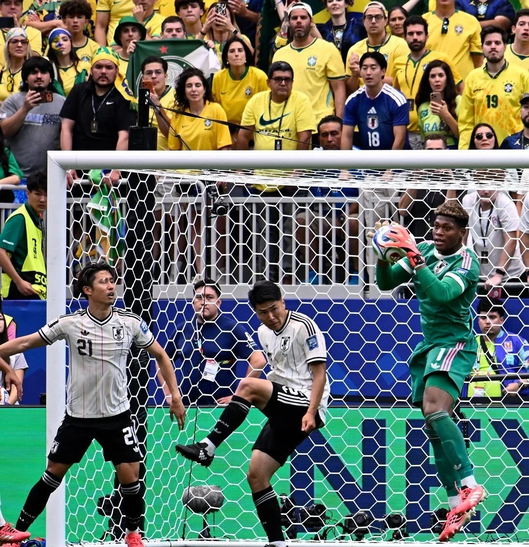 Japanese goalkeeper, Zion Suzuki, makes a catch in front of a section of Brazil fans, as Hiroki Ito and Junnoske Suzuki watch on
