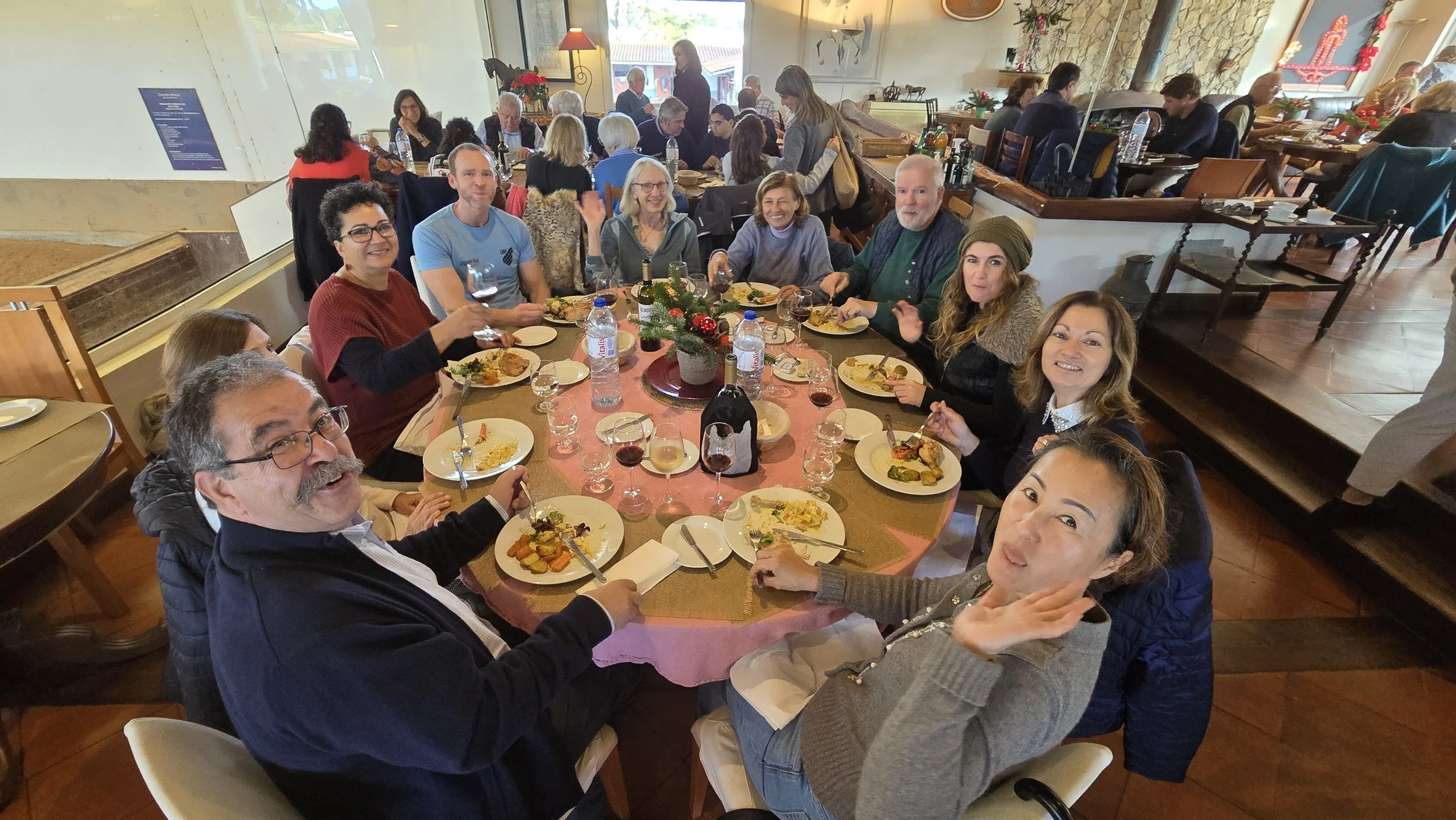 A group of people enjoying a meal together at a round table in a restaurant, with a decorated centerpiece and various dishes and drinks on the table.