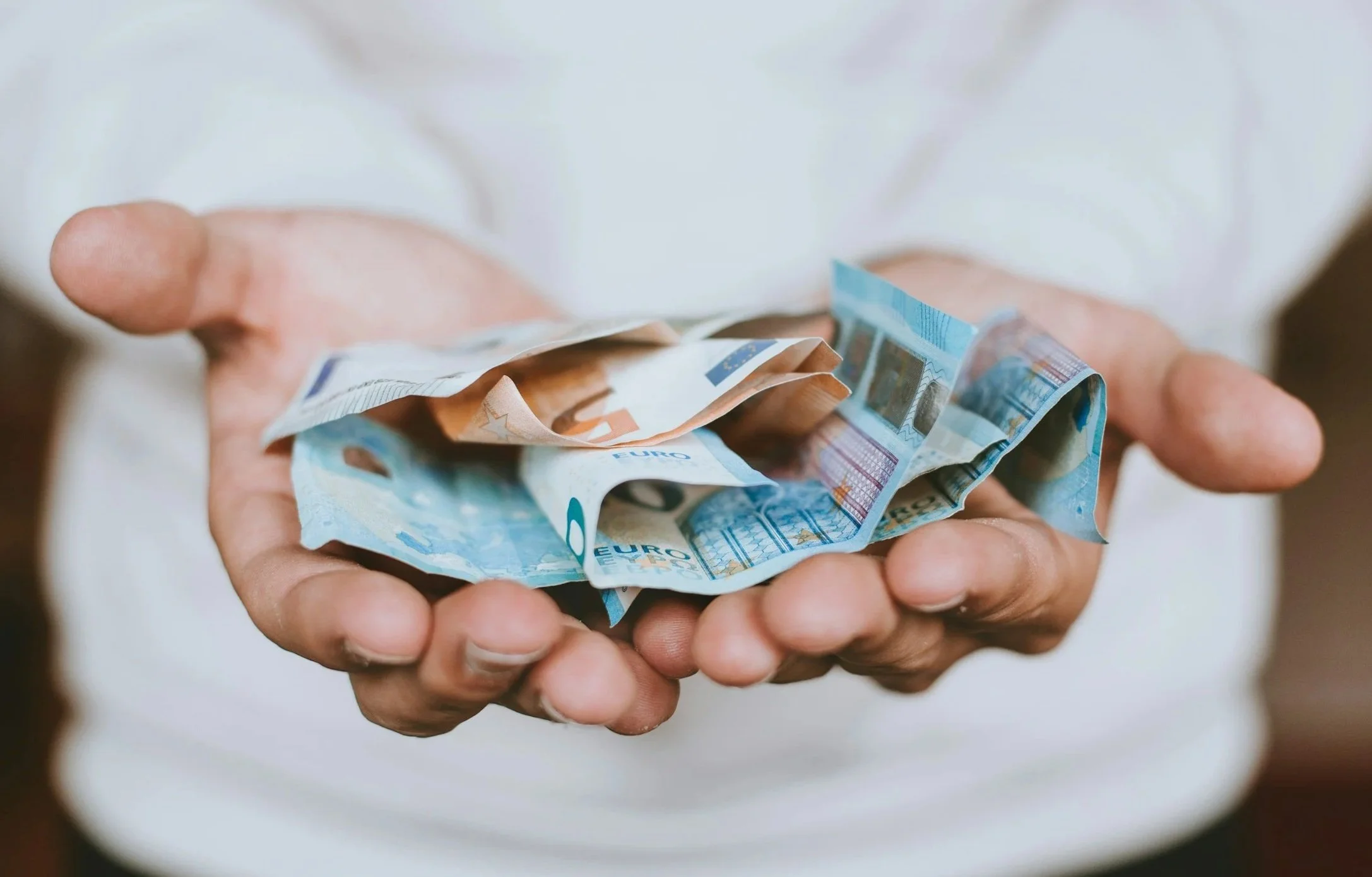 Person holding crumpled euro banknotes in their hands.
