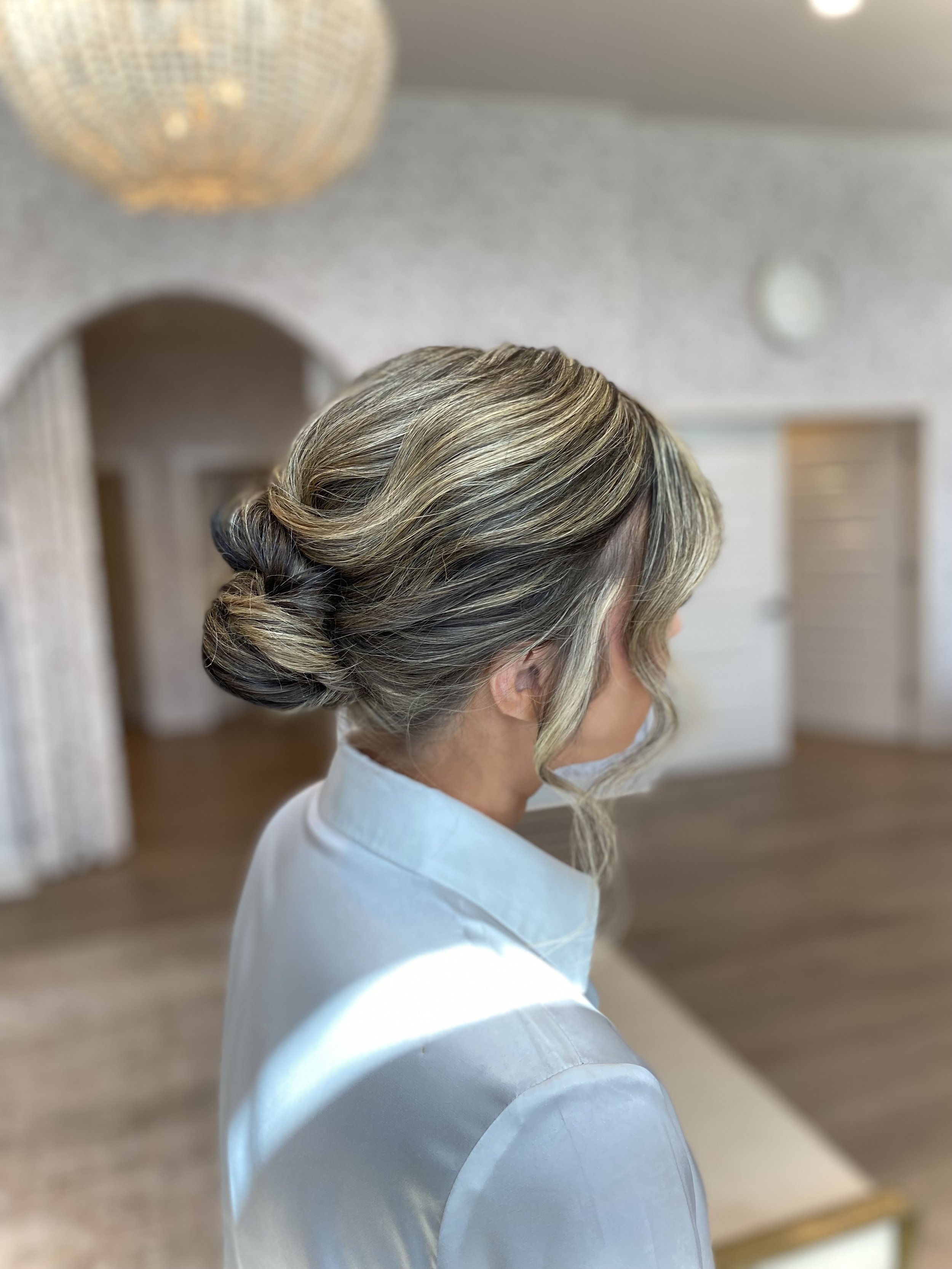 Elegant updo hairstyle with blonde streaks on gray hair, worn with a white garment and a face mask.
