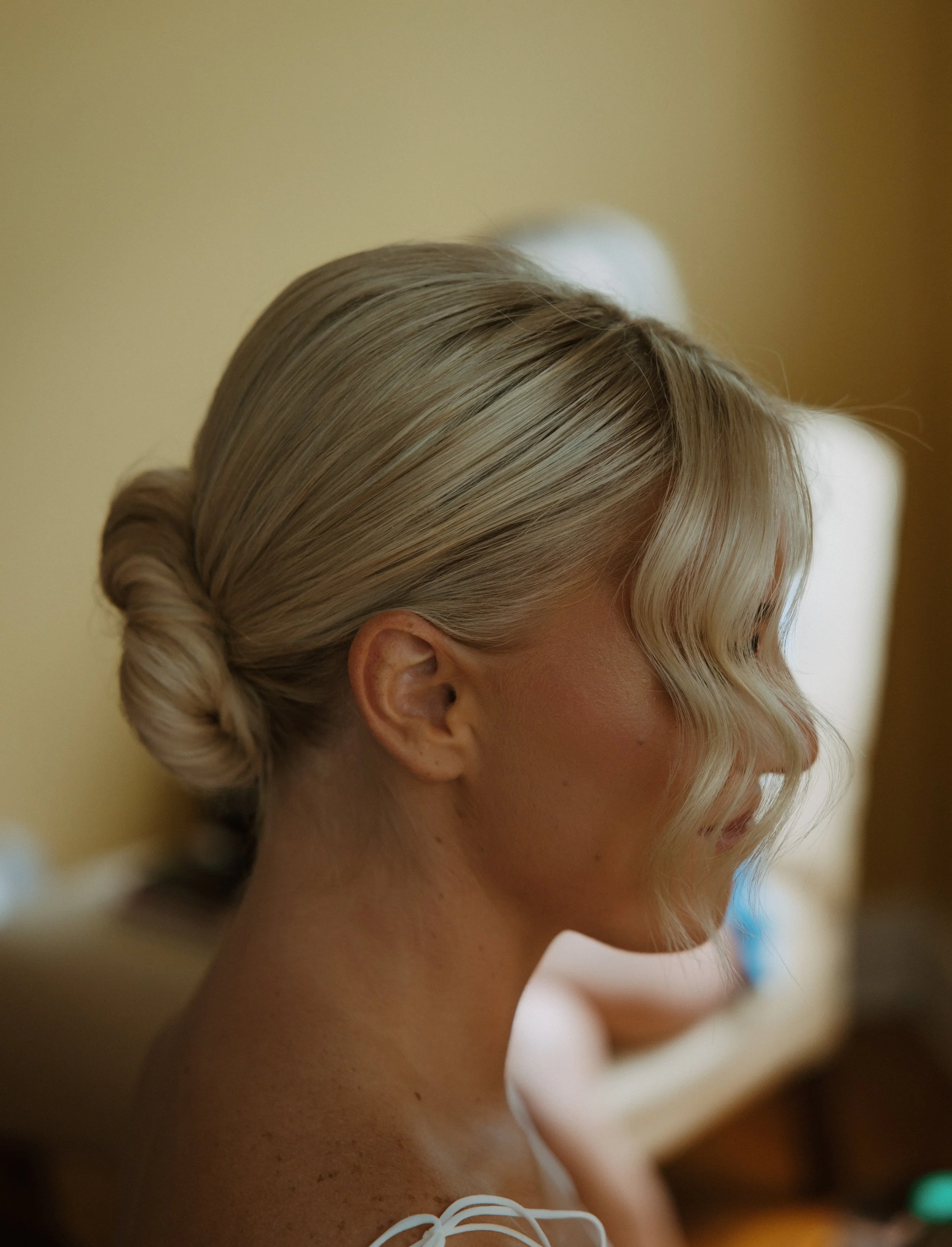 Close-up of a woman with blonde hair styled in an elegant updo and soft curls framing her face, in a well-lit indoor setting.