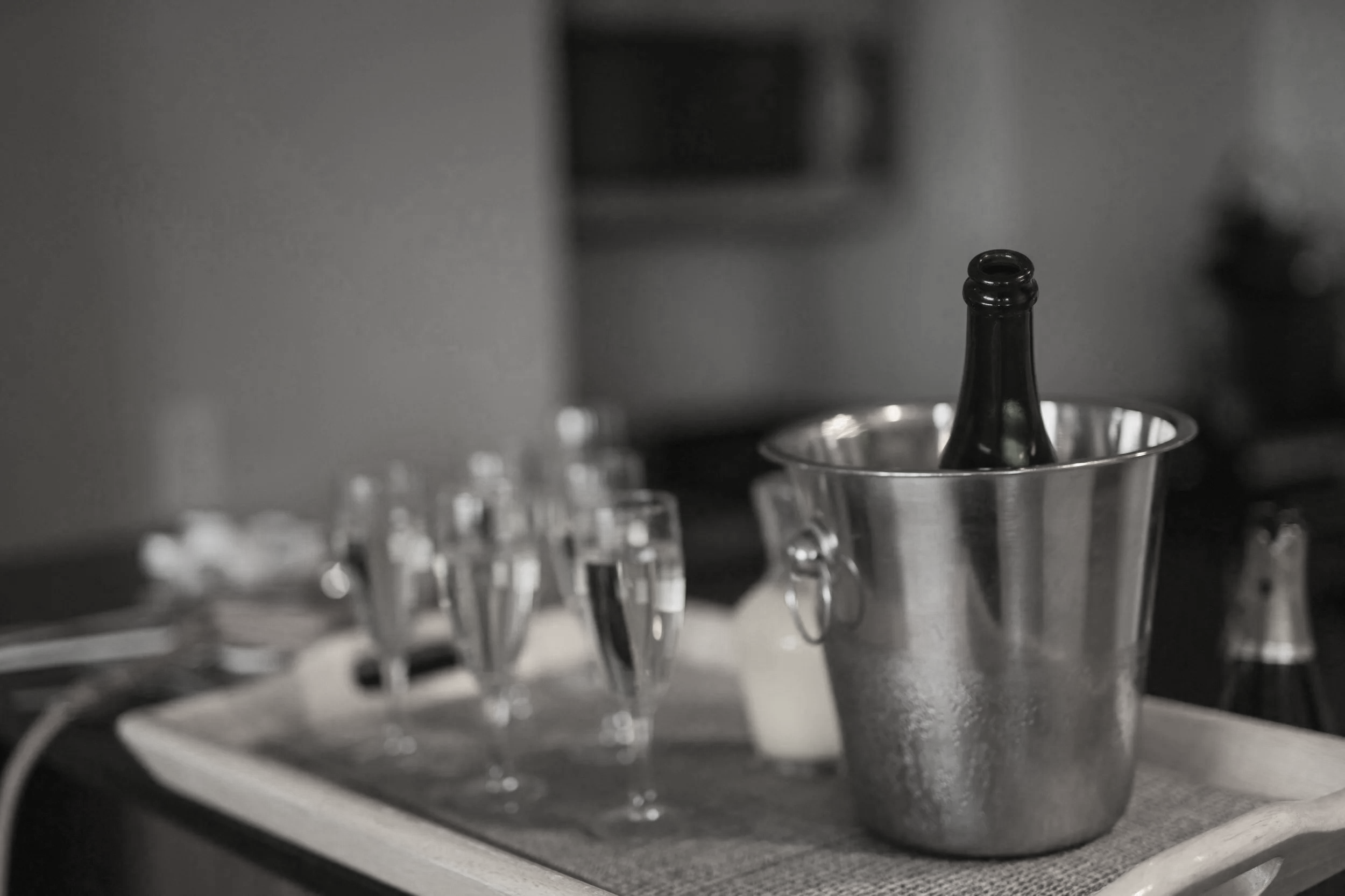 Close-up of an empty glass bottle in a metal ice bucket on a bar counter with blurred glasses and bottles in the background.