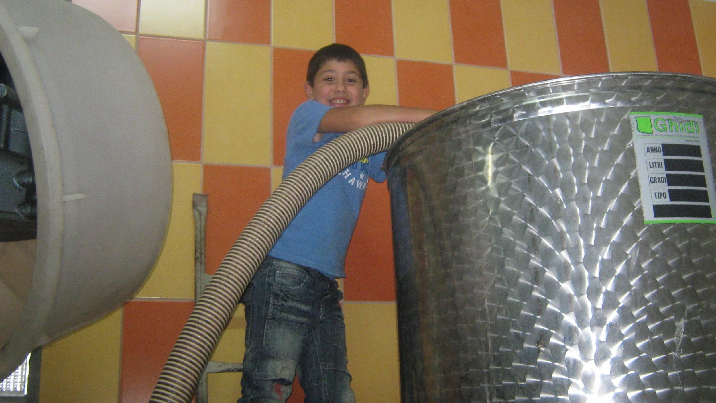 Un ragazzino con una maglietta blu sorride mentre si arrampica su una superficie di metallo in un ambiente con pareti a quadretti gialli e arancioni.