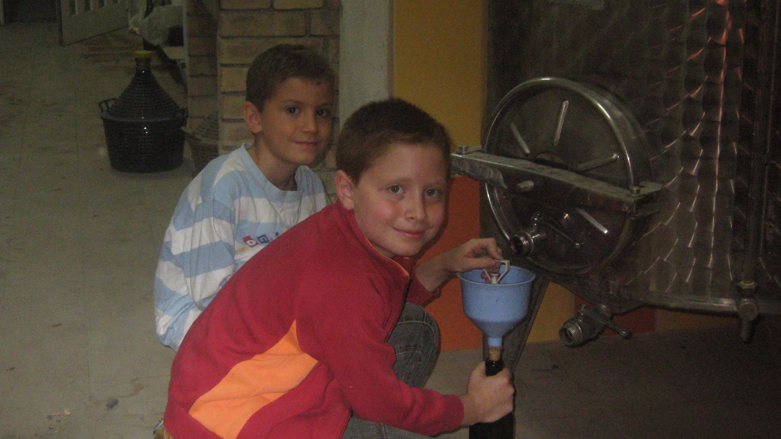 Due bambini riempiono un contenitore di plastica con olio da una macchina di gelato a turbina in un ambiente interno.
