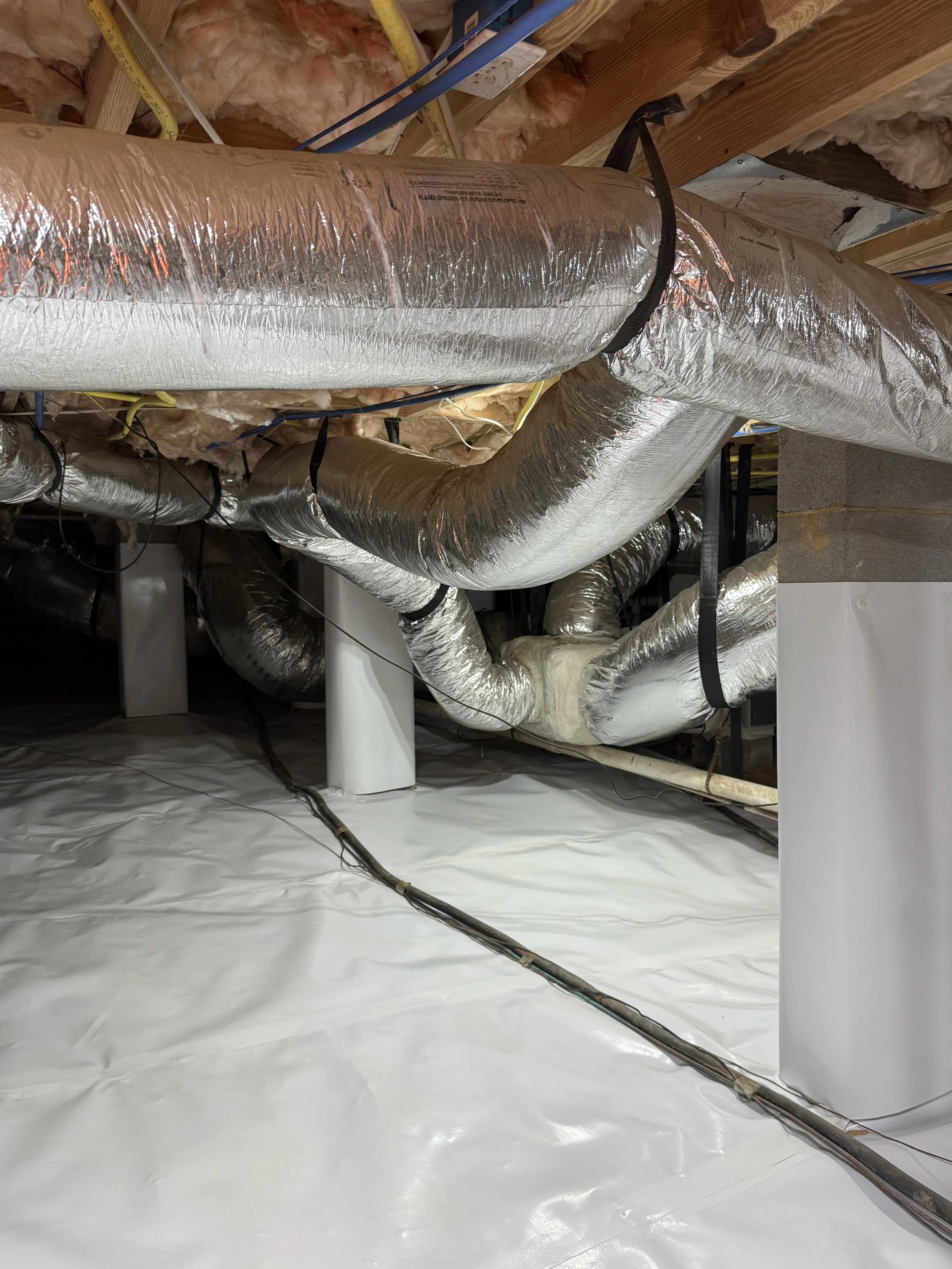 Insulation and HVAC ducts in a building's ceiling area, with silver ductwork, electrical wiring, and wooden framing.