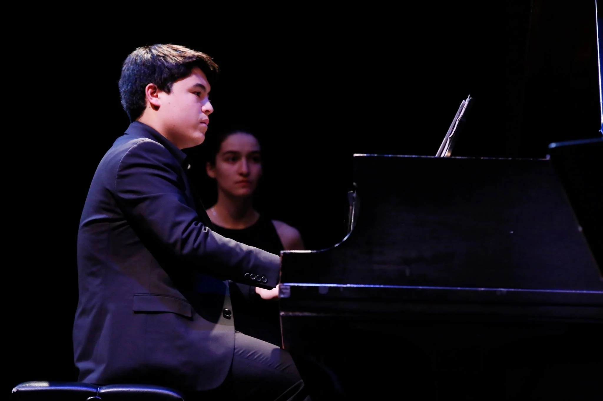 Young man playing piano on stage with a woman in background