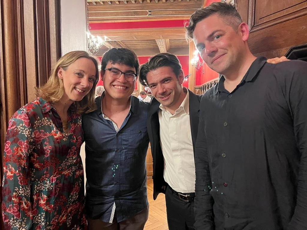 Four people smiling and posing for a photo at an indoor event with wooden walls and chandeliers.