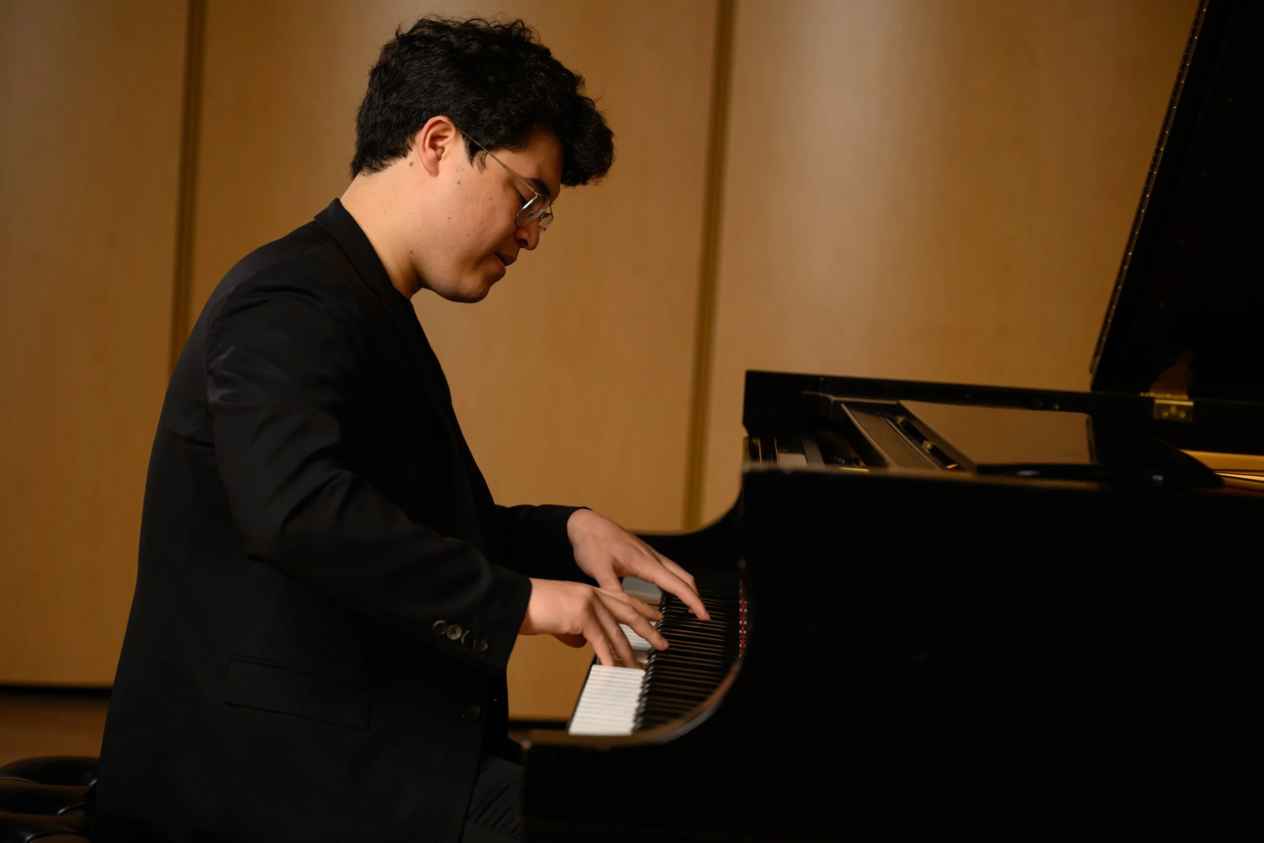 A young man playing a grand piano in a music room.