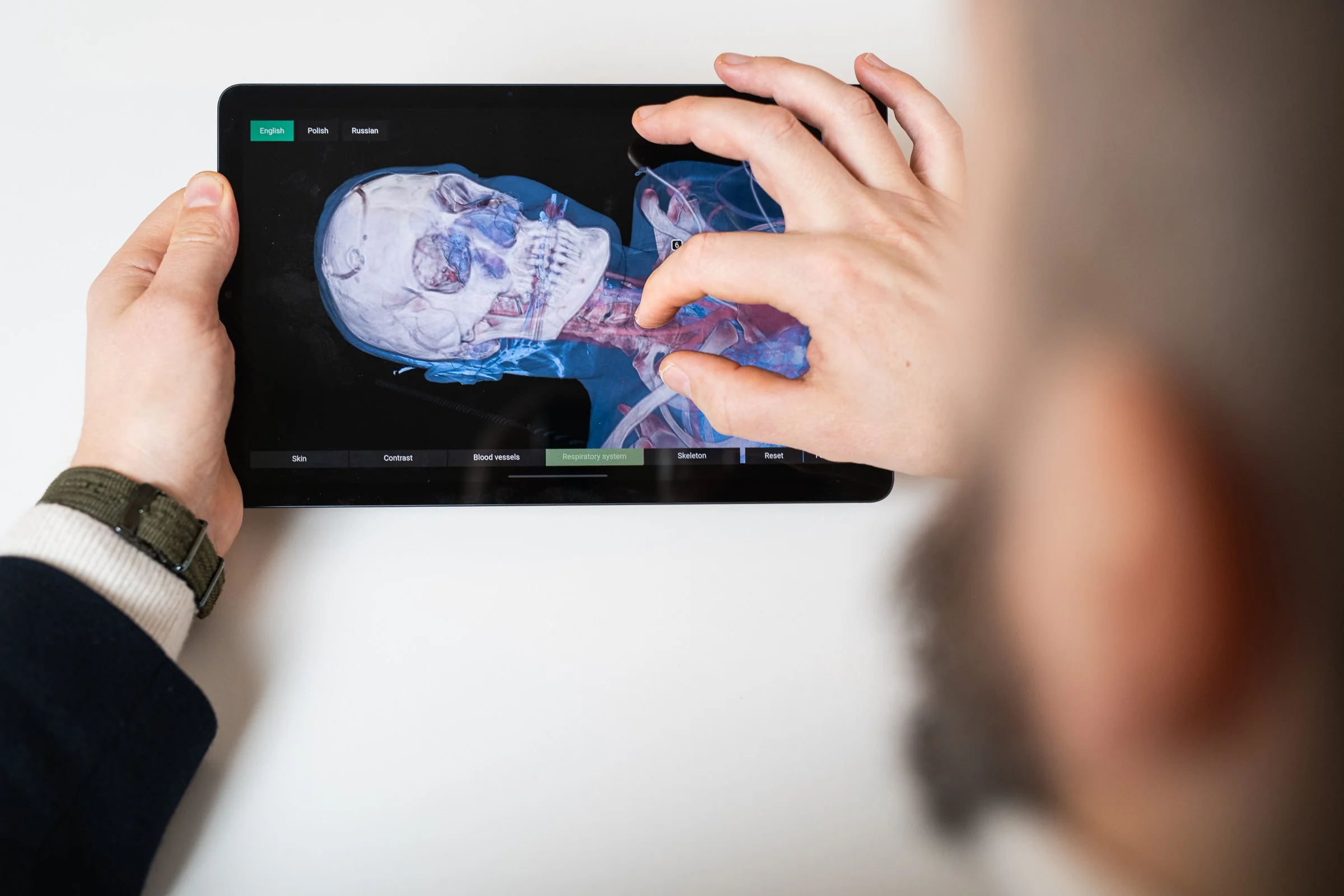Person holding a tablet displaying a 3D medical scan of a human skull and respiratory system, with touch controls at the bottom.