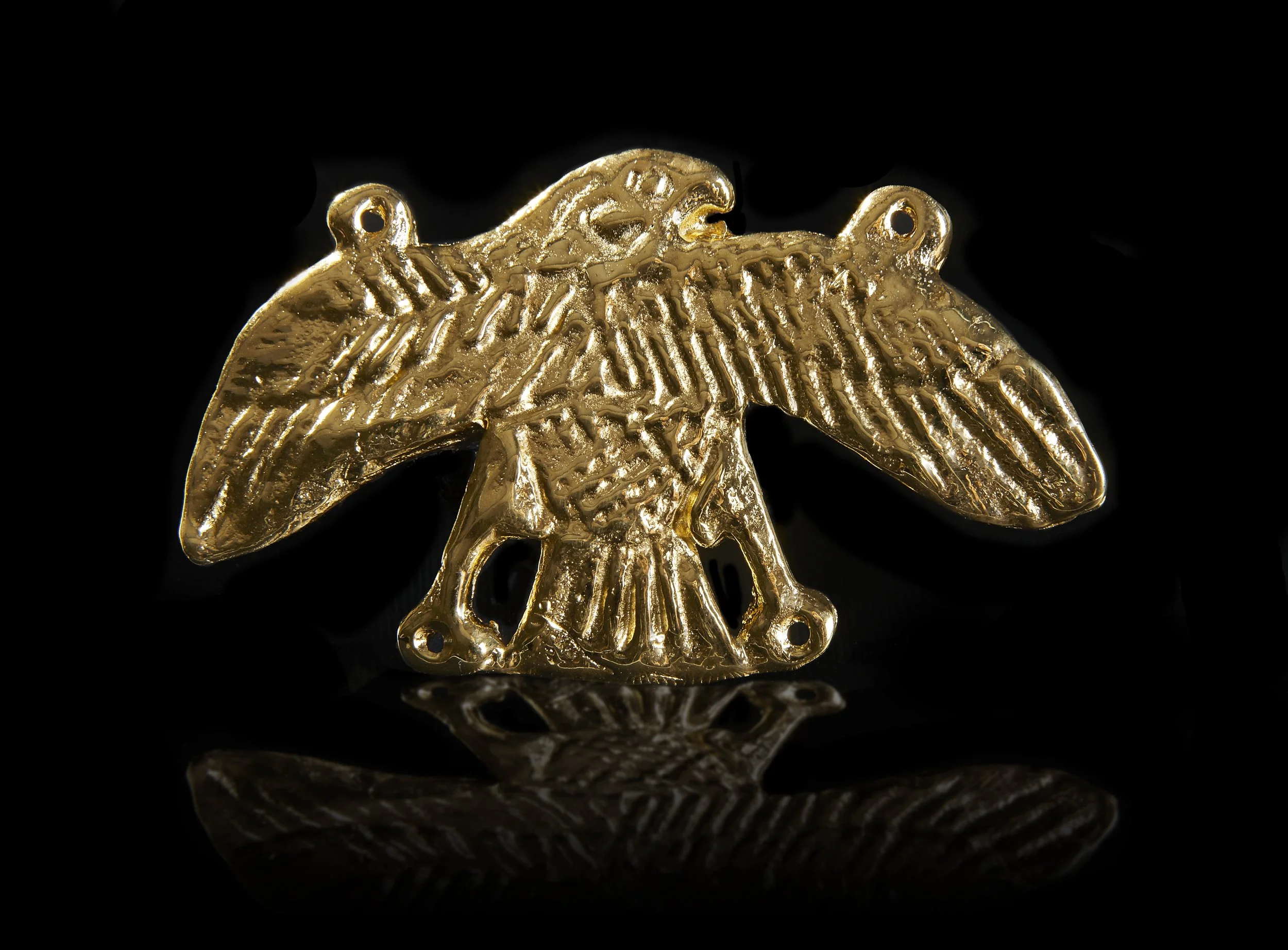 A gold-colored jewelry charm in the shape of an owl with detailed feathers and two small holes at the top for attaching to a necklace or bracelet.