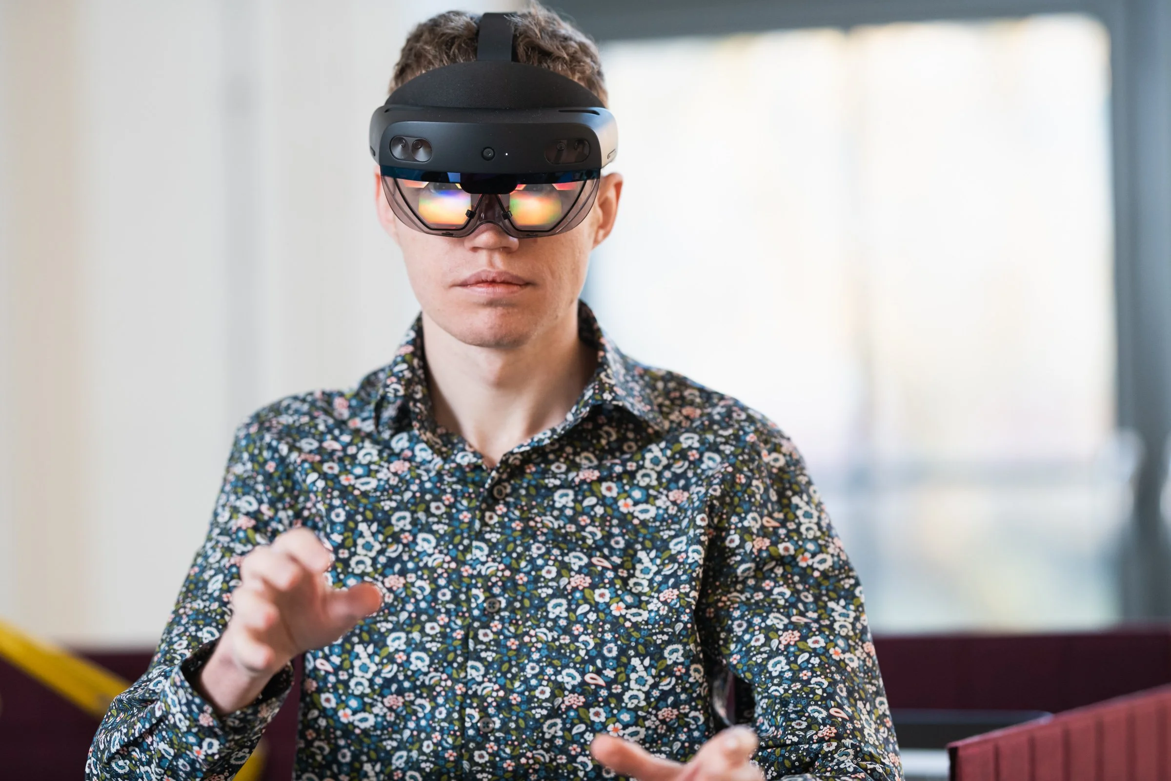 A man wearing a floral shirt using a virtual reality headset and controllers.