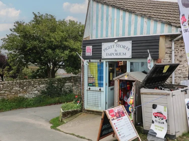 Exterior of Piglet Stores & Emporium selling ice cream and beverages, with signs for cold beer and a menu board outside.