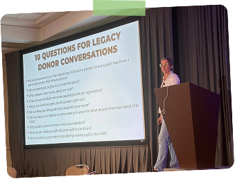 A woman presenting on stage next to a large screen displaying the title "10 Questions for Legacy Donor Conversations." The presentation slide lists questions related to donor engagement.