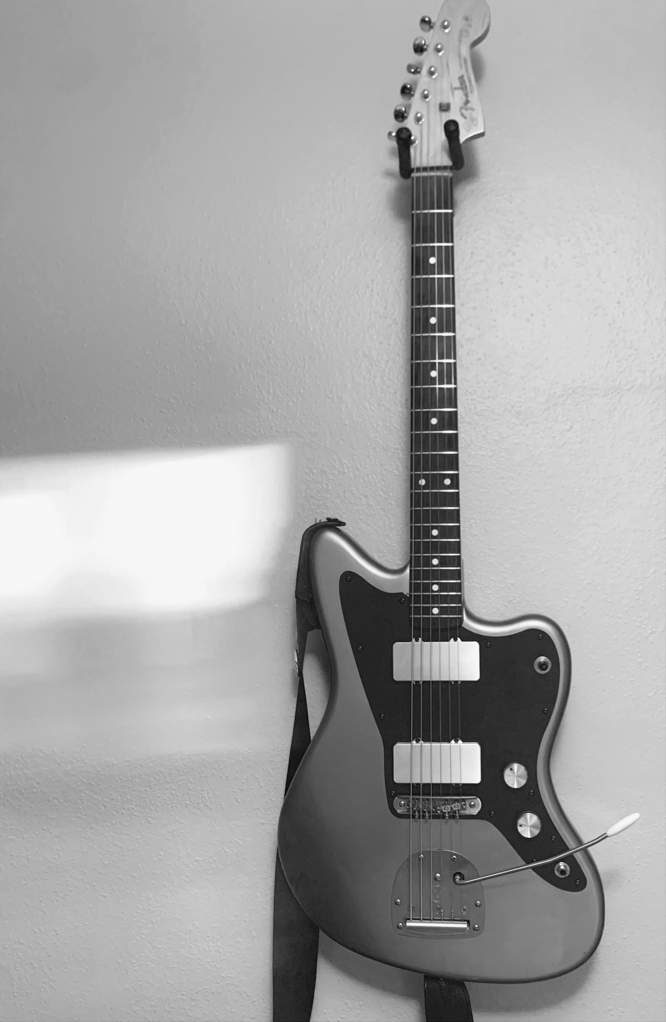 Black and white photo of an electric guitar hanging on a wall.