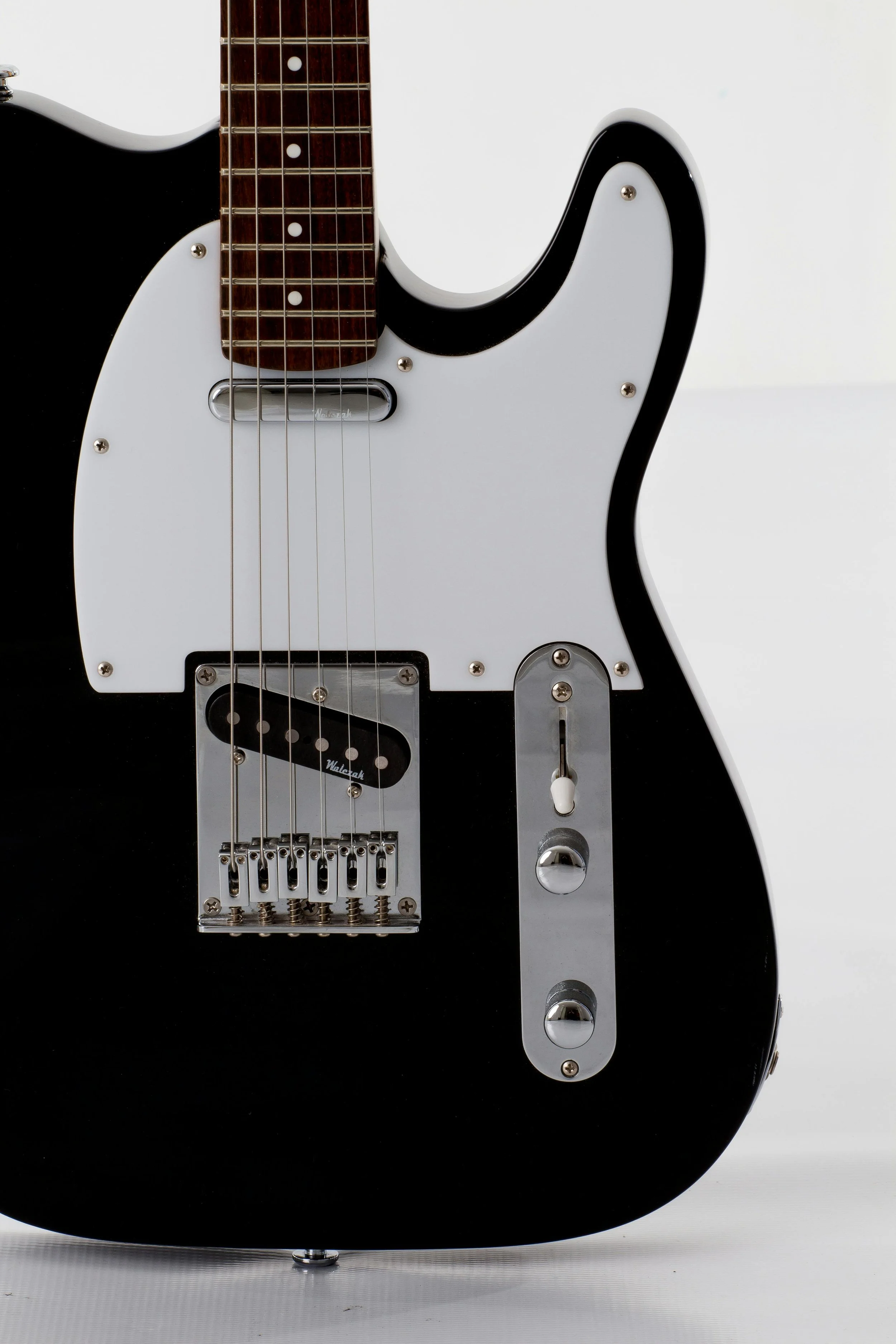 Close-up of a black and white electric guitar with a white pickguard, a chrome bridge, and control knobs.