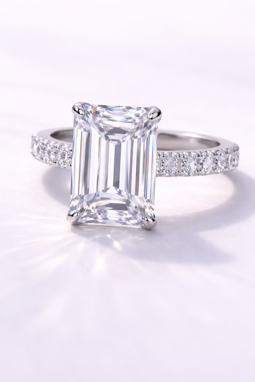 Close-up of a diamond ring with a large rectangular emerald-cut diamond and a band of smaller diamonds, on a soft white background.