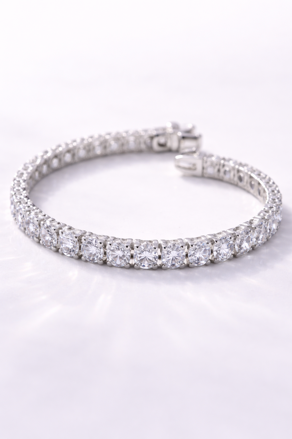 A silver bracelet encrusted with clear gemstones, laid on a white surface.