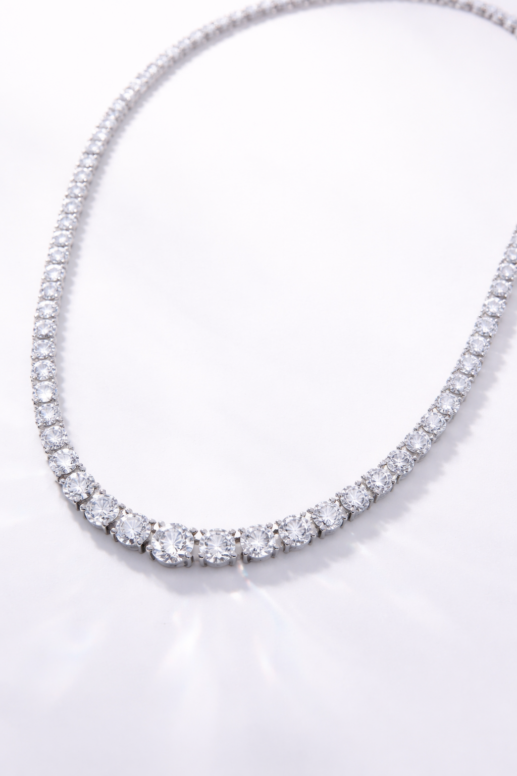 A diamond tennis necklace arranged in a curved shape on a white background.
