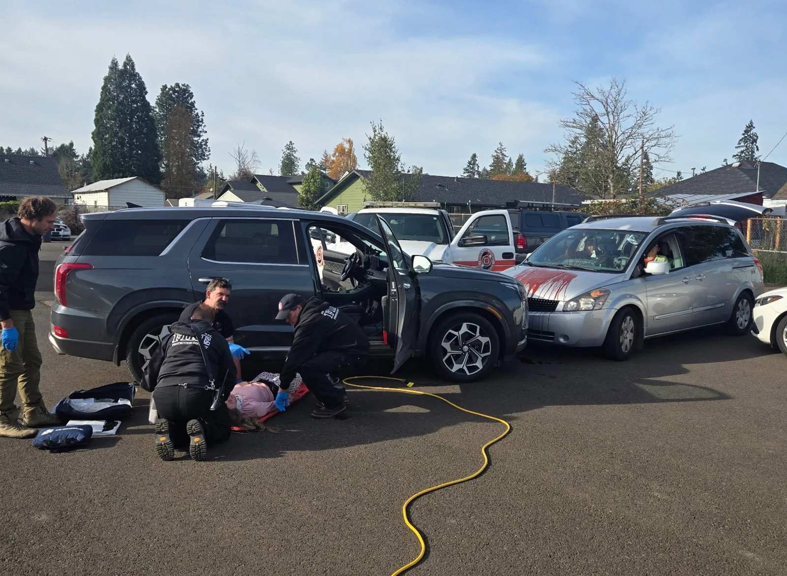 Emergency responders attending to a person lying on the ground near a black SUV involved in a crash, with other parked cars in the background.