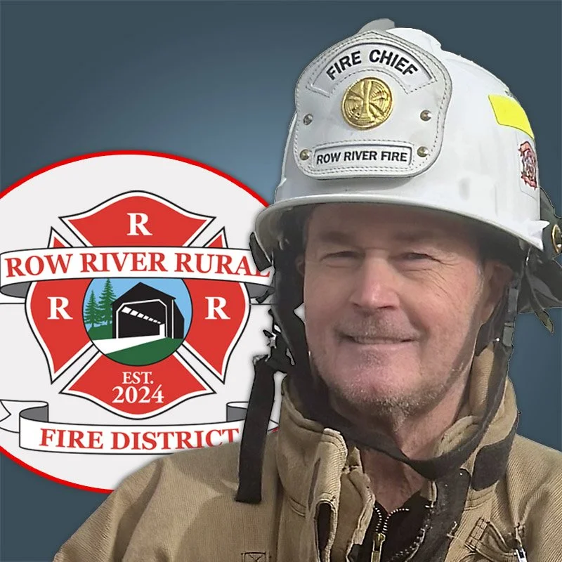 A firefighter wearing a white helmet with a badge labeled 'Fire Chief' and 'Row River Fire,' alongside a fire district emblem that reads 'Row River Rural Fire District, Est. 2024.'
