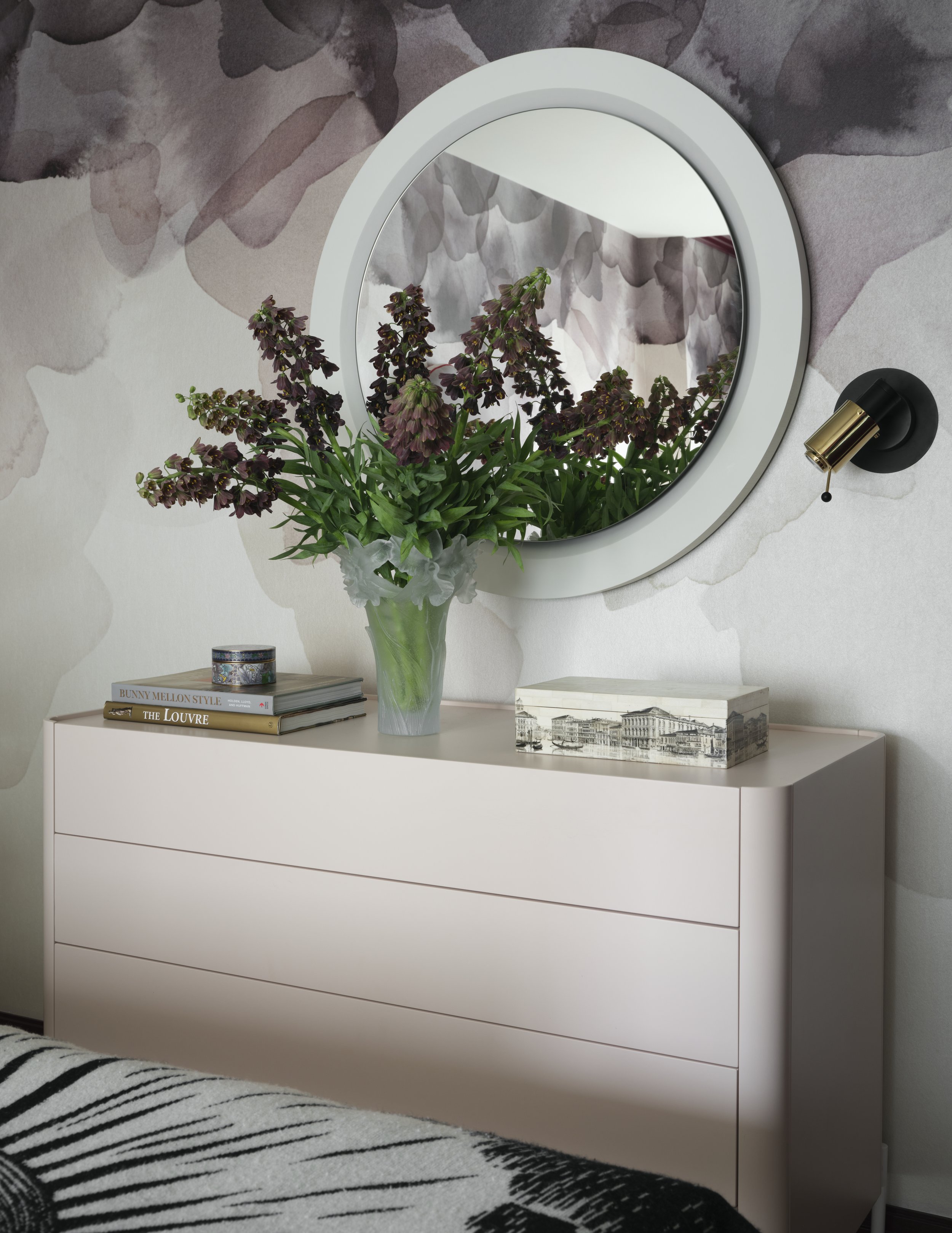 Light pink dresser in bedroom with round mirror mounted on the wall