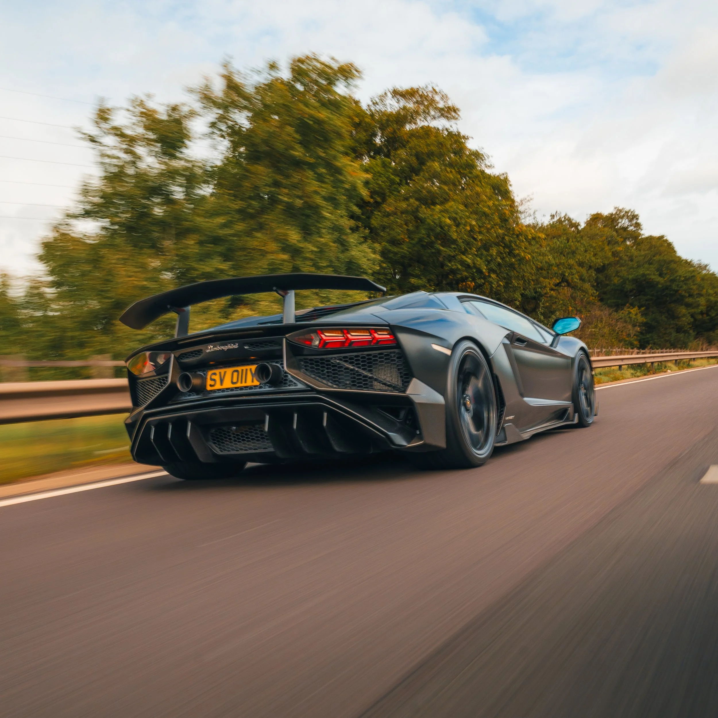 A black Lamborghini sports car driving on a highway with trees in the background.