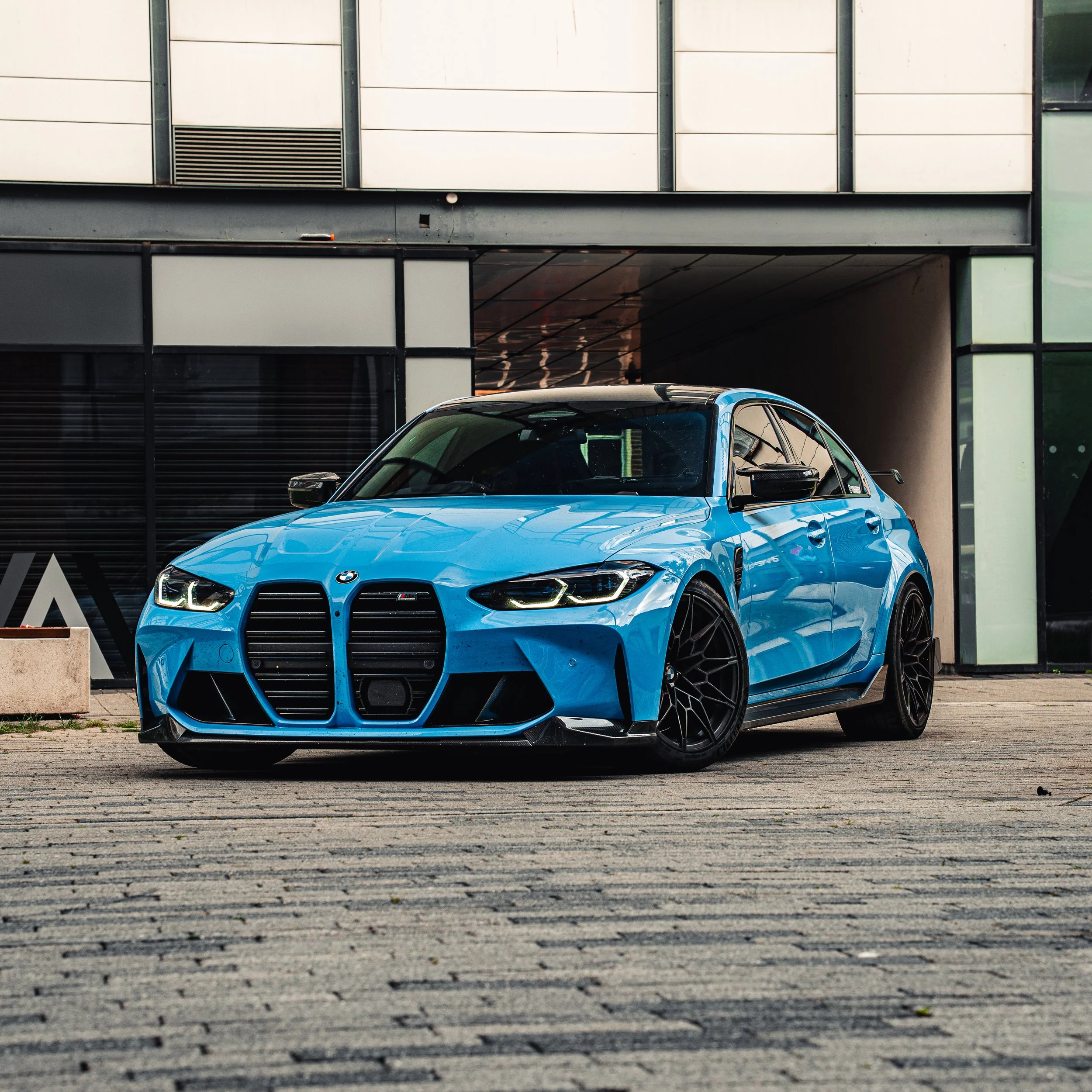 A blue BMW car parked outside a modern building with large windows and a garage entrance.