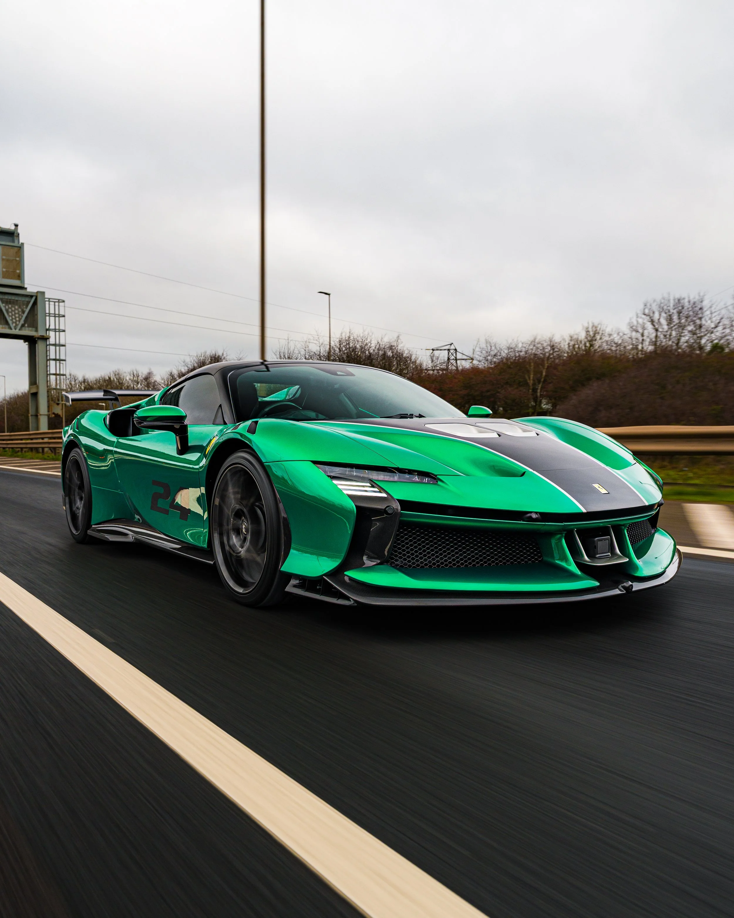 A green and black sports car driving on a highway under a cloudy sky.