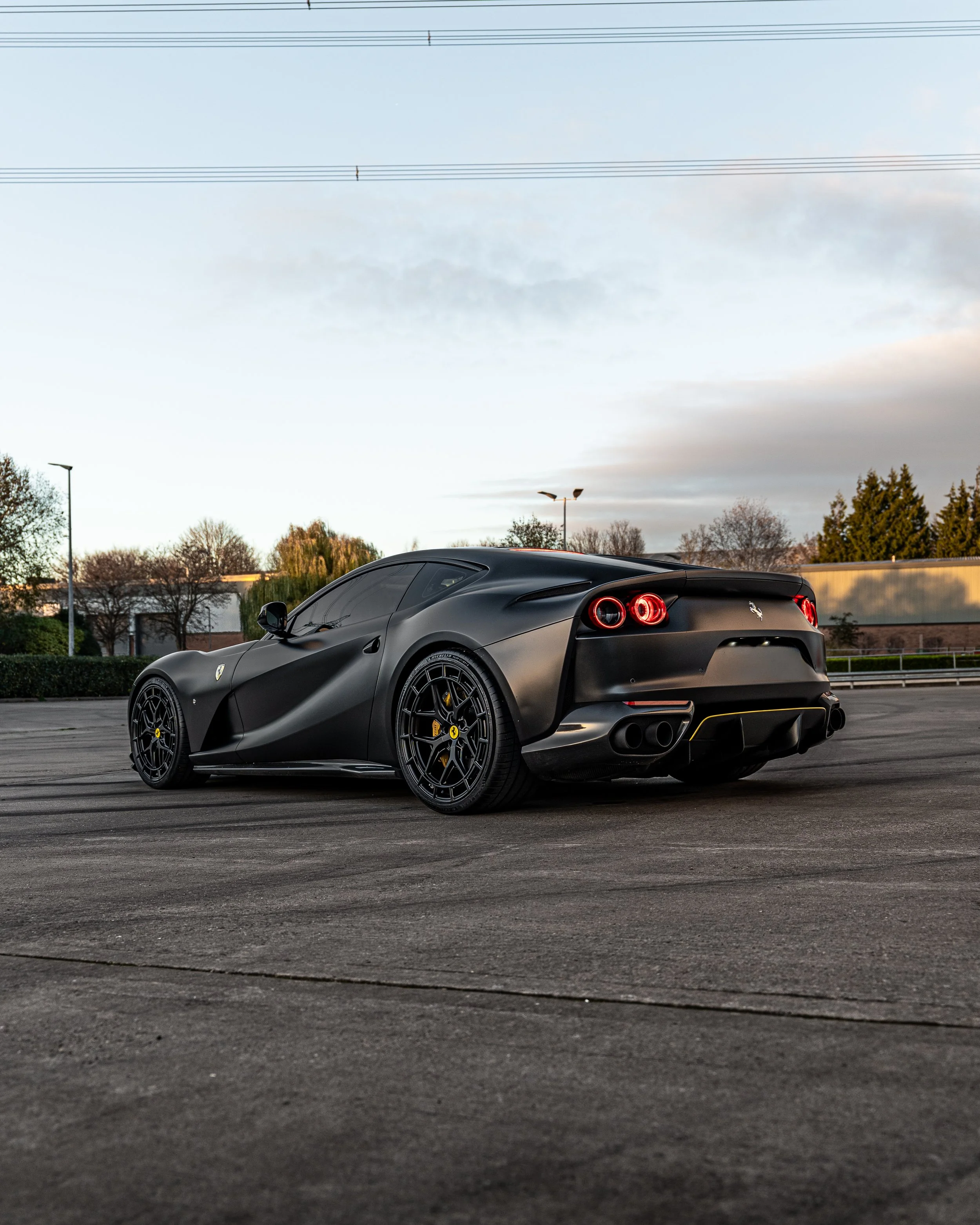A matte black Ferrari sports car parked in an open lot during sunset.