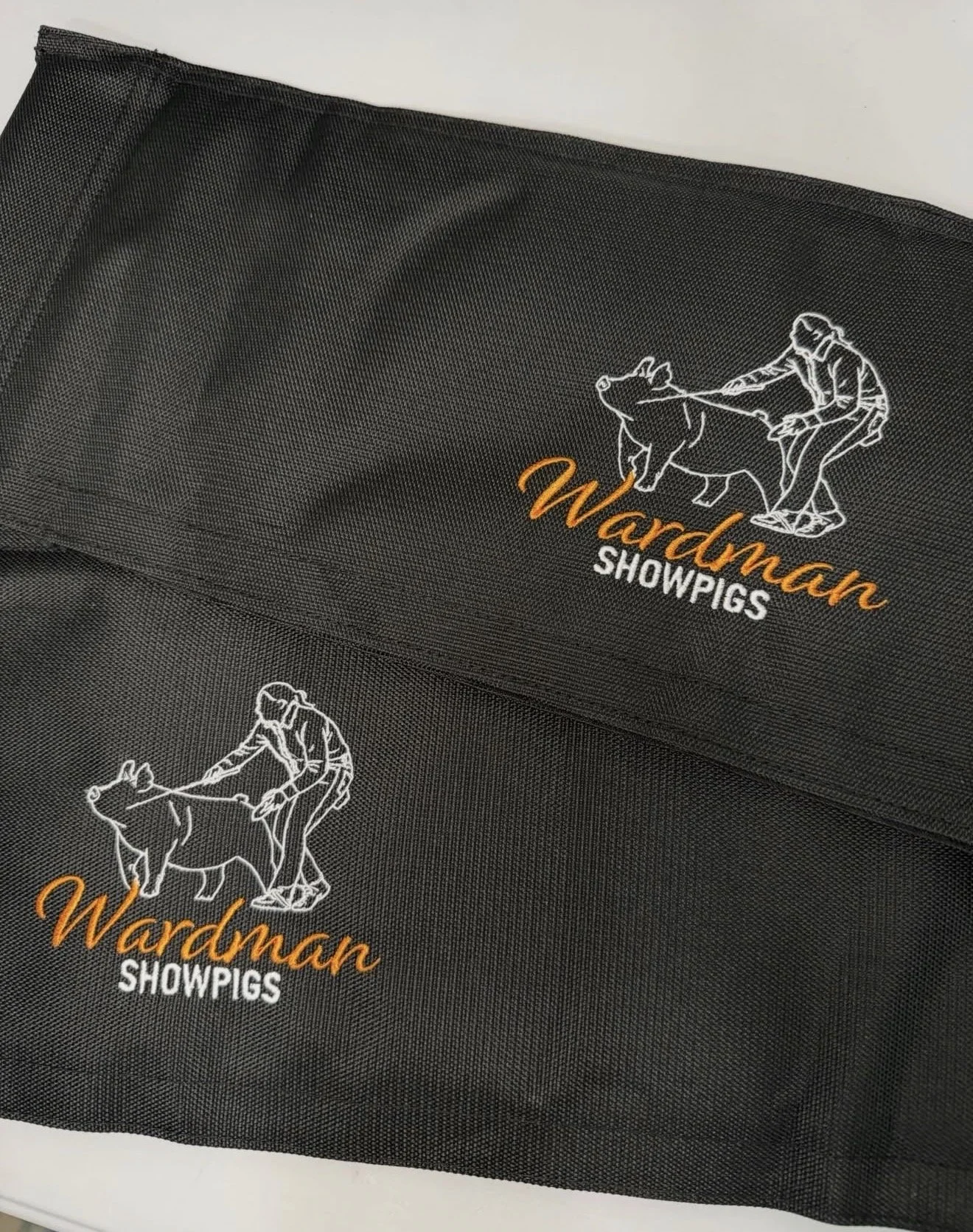 Black show pig equipment bag with embroidered outline of a pig and a person in a cowboy hat leaning on the pig, alongside the text "Warman SHOWPIGS" in orange and white.
